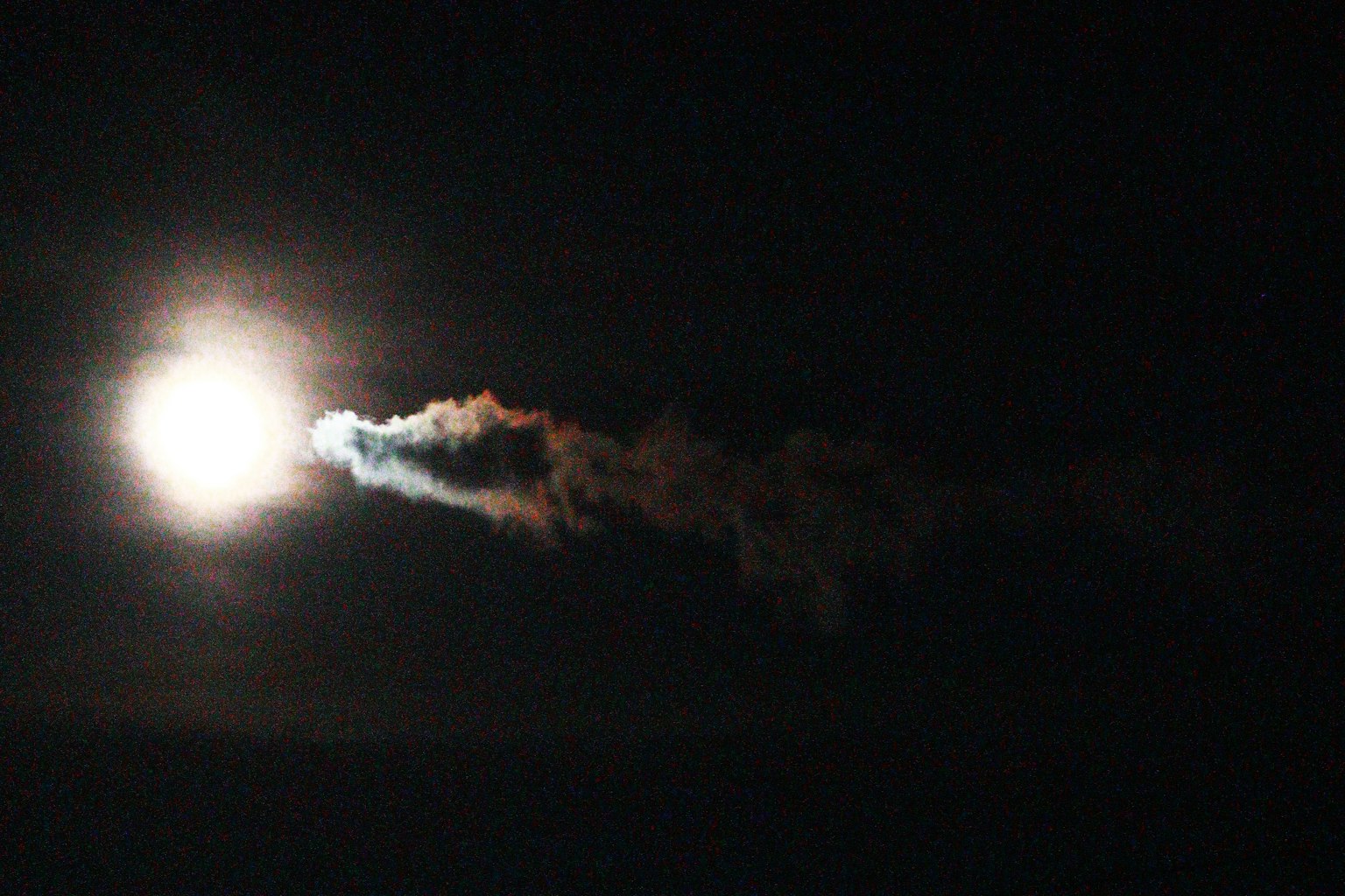 夜空に浮かぶ明るい月とその後ろに広がる煙の軌跡