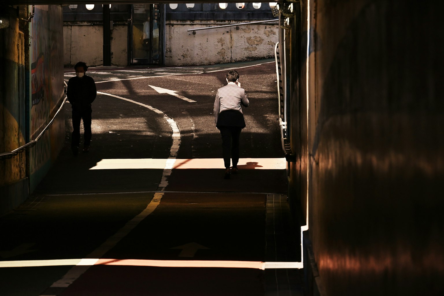 Siluetas de dos personas en un túnel con luz solar proyectando sombras
