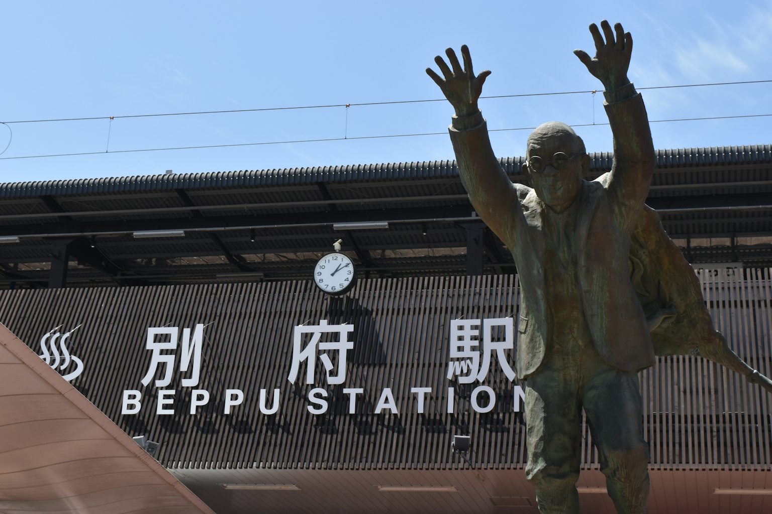Statue vor dem Bahnhof Beppu mit Uhr und Beschilderung