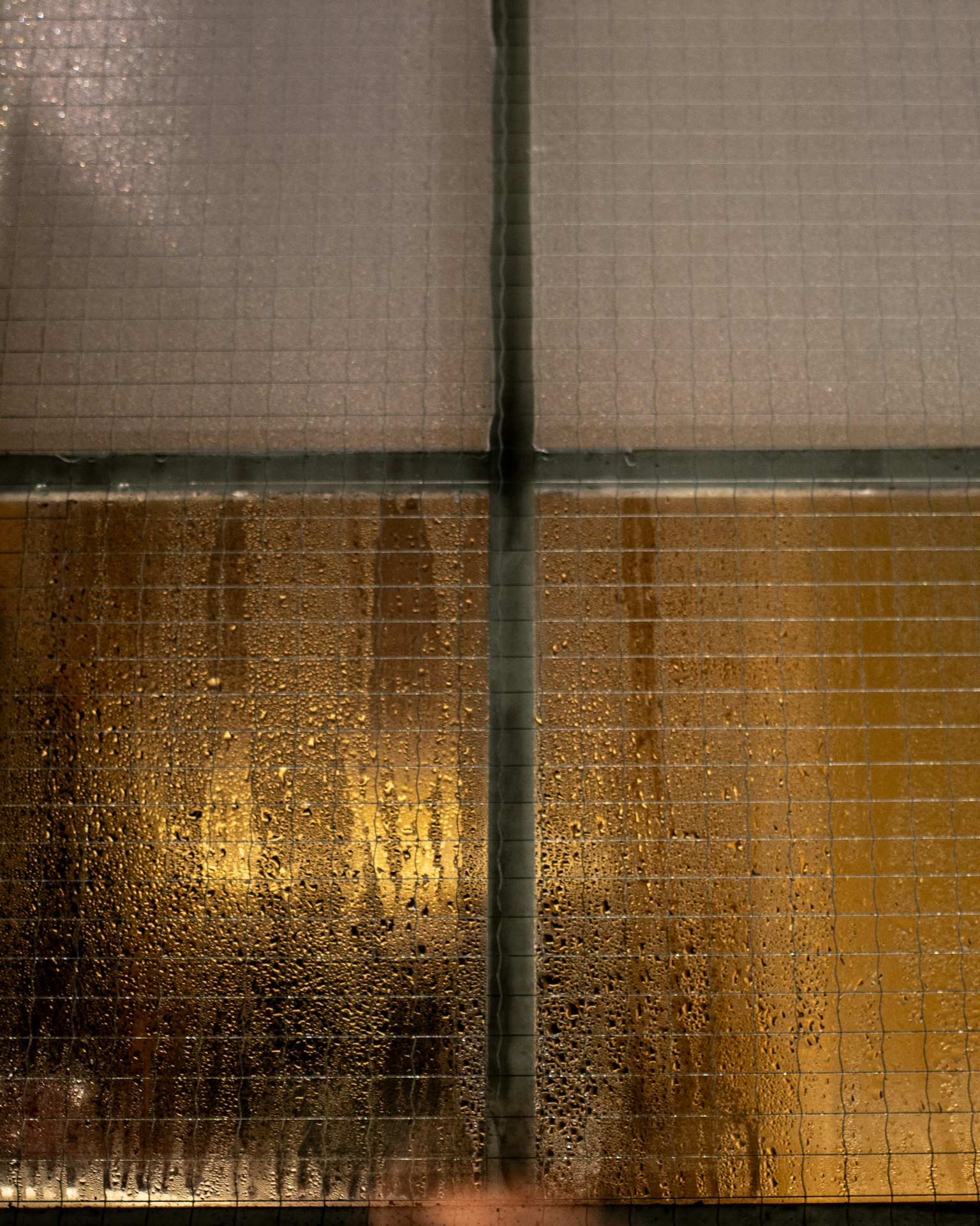 Immagine di un pannello di vetro quadrato con gocce d'acqua la parte superiore è trasparente e la parte inferiore riflette una luce dorata