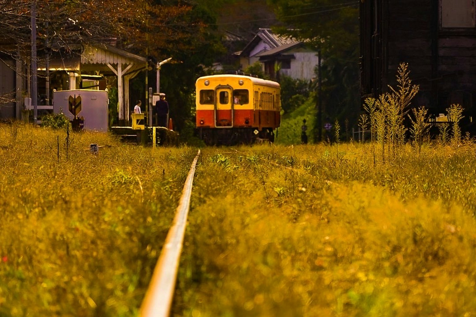 Ein Vintage-Zug auf einem grasbewachsenen Gleis mit einem Bahnhof im Hintergrund