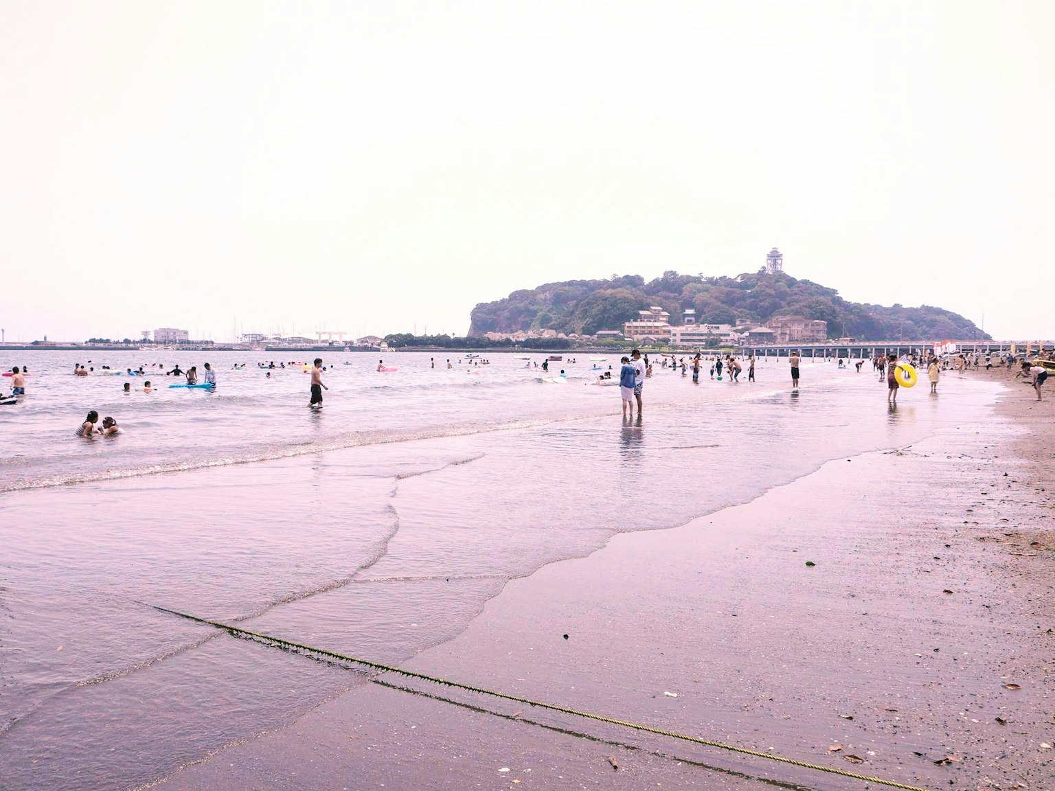 Orang-orang menikmati pantai dengan pemandangan bukit di kejauhan
