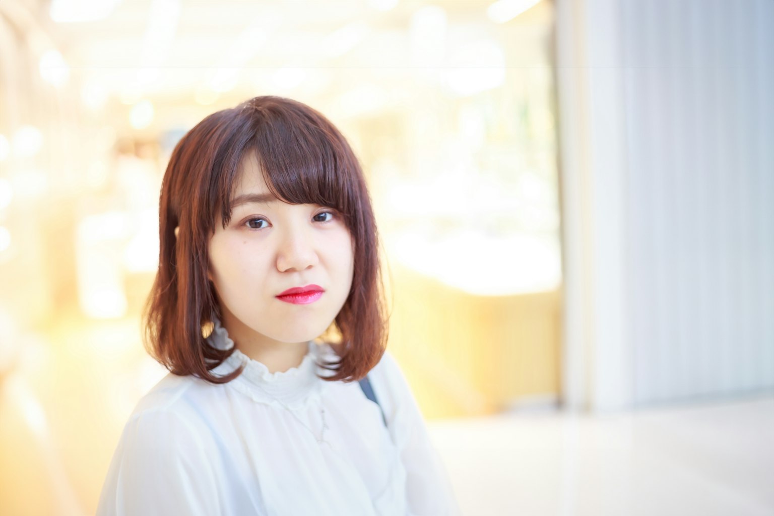 Portrait d'une femme souriante contre un fond lumineux avec des cheveux au carré et portant un élégant chemisier bleu
