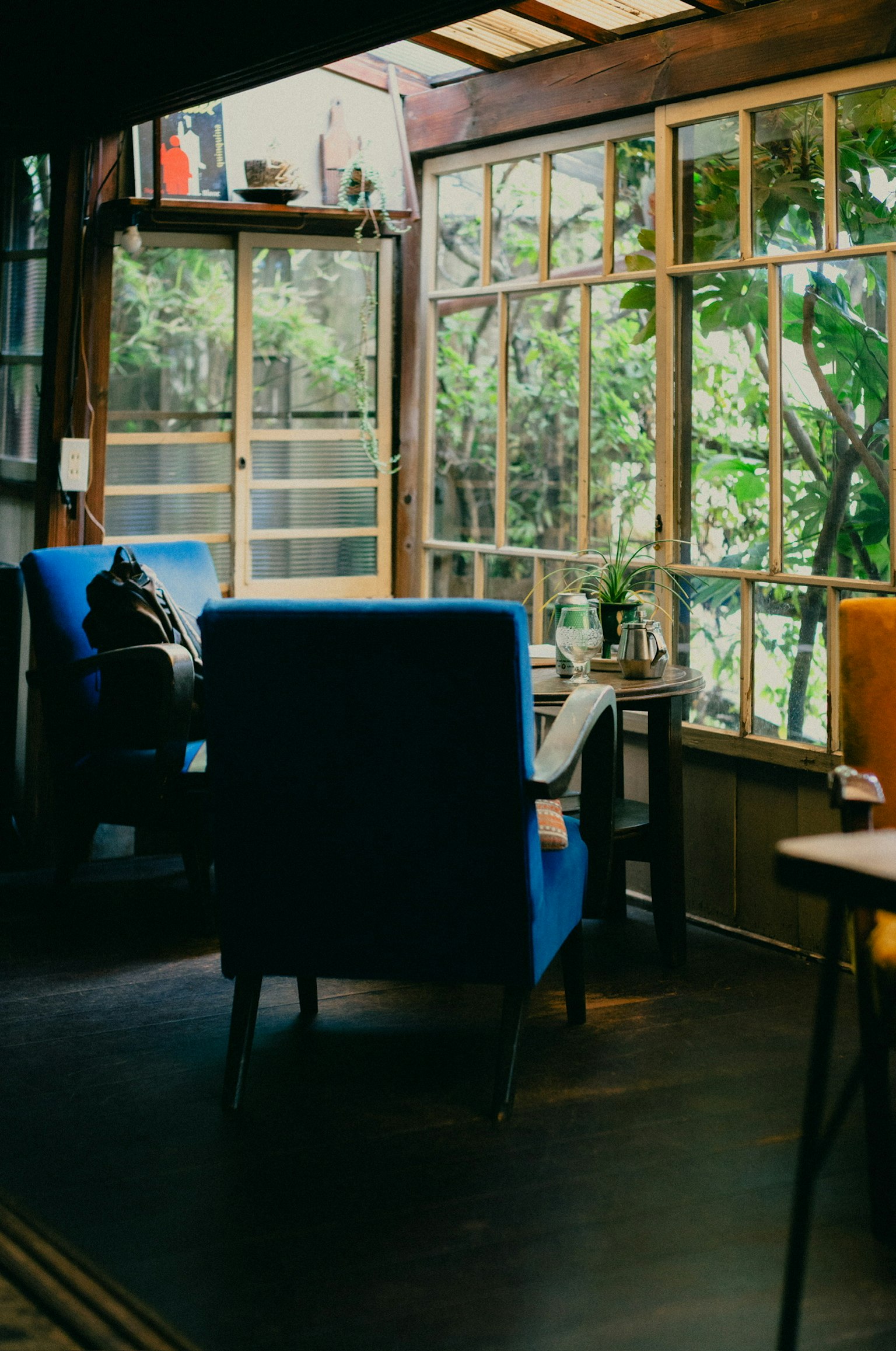青い椅子と木製のテーブルがあるカフェの内部 緑の植物が見える大きな窓