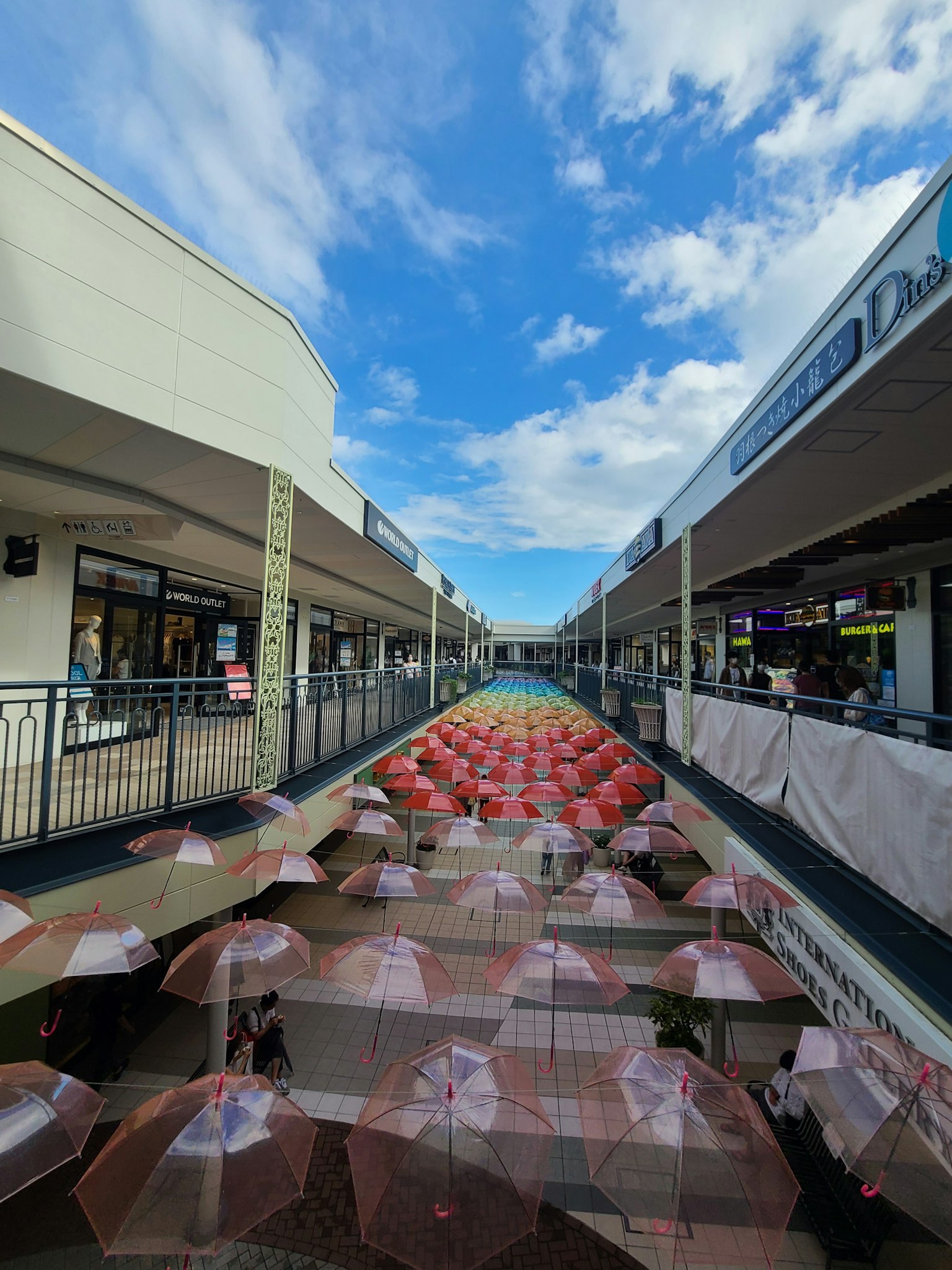 Corridoio di un centro commerciale con ombrelli artistici sotto un cielo azzurro