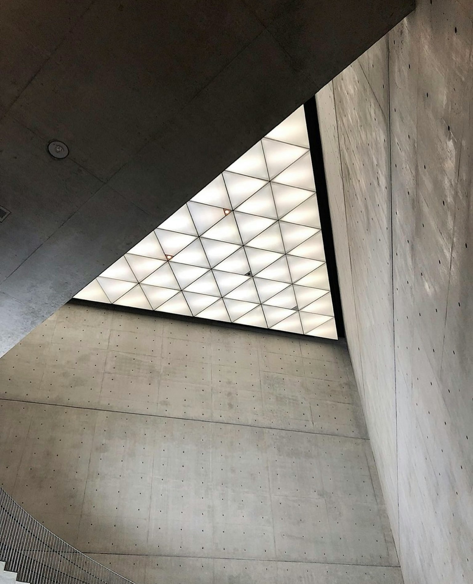 Blick von einer Treppe nach oben auf ein dreieckiges Decken-Design und Betonwände