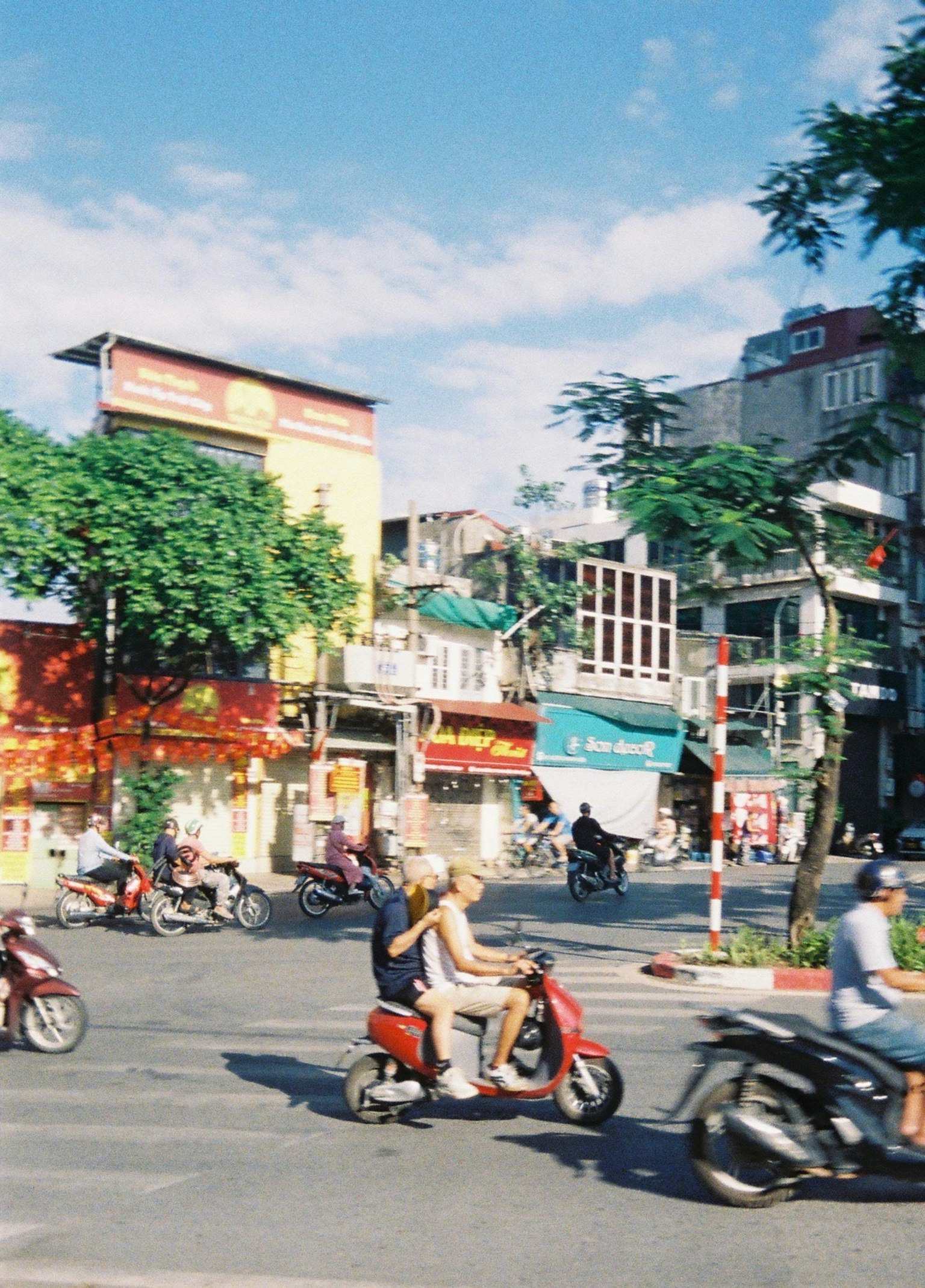 バイクが行き交う賑やかな交差点の風景 店舗の看板と青空が広がる