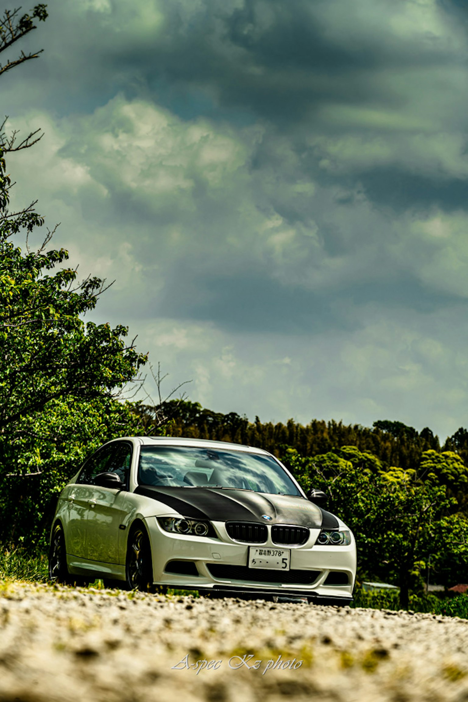 White BMW parked on a gravel road surrounded by green trees