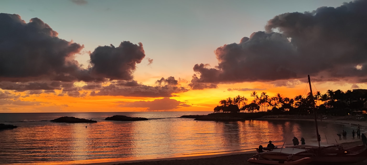 Splendida scena di spiaggia con un tramonto mozzafiato palme e persone sulla riva