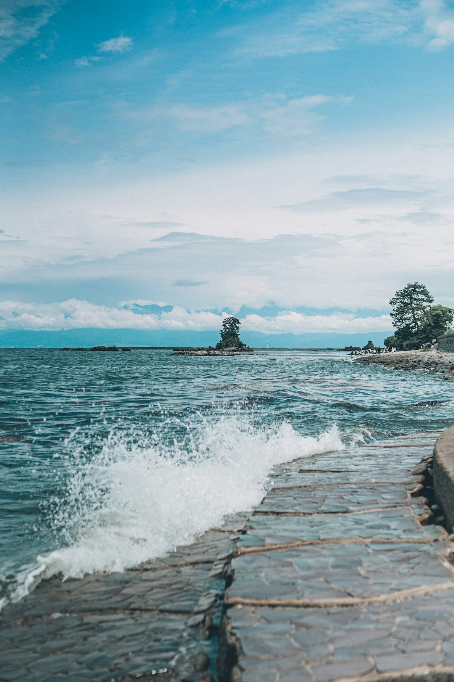 Stone pier under a blue sea and sky with waves crashing