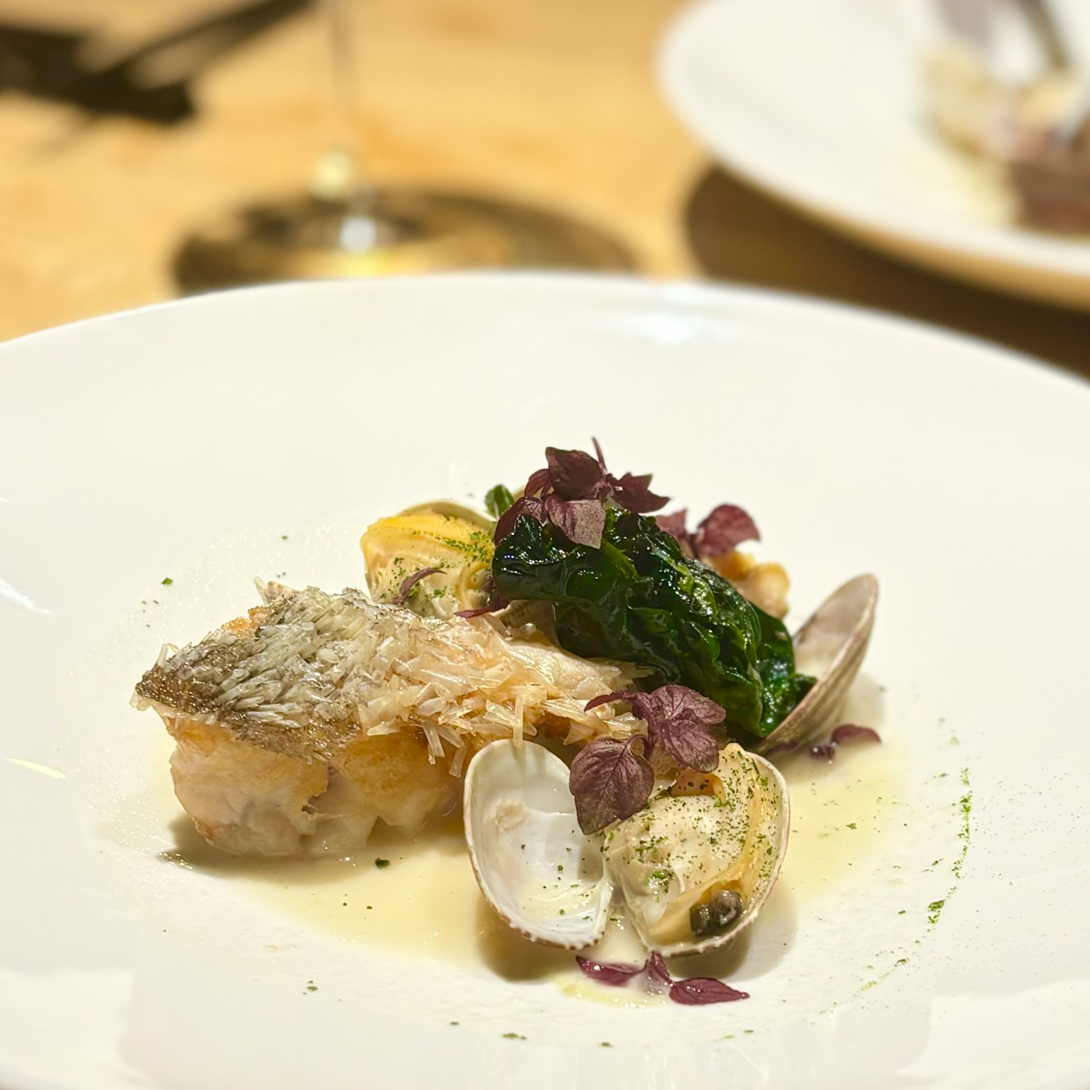 Un plat magnifiquement dressé avec du poisson grillé et des palourdes garni d'épinards frais et d'herbes violettes