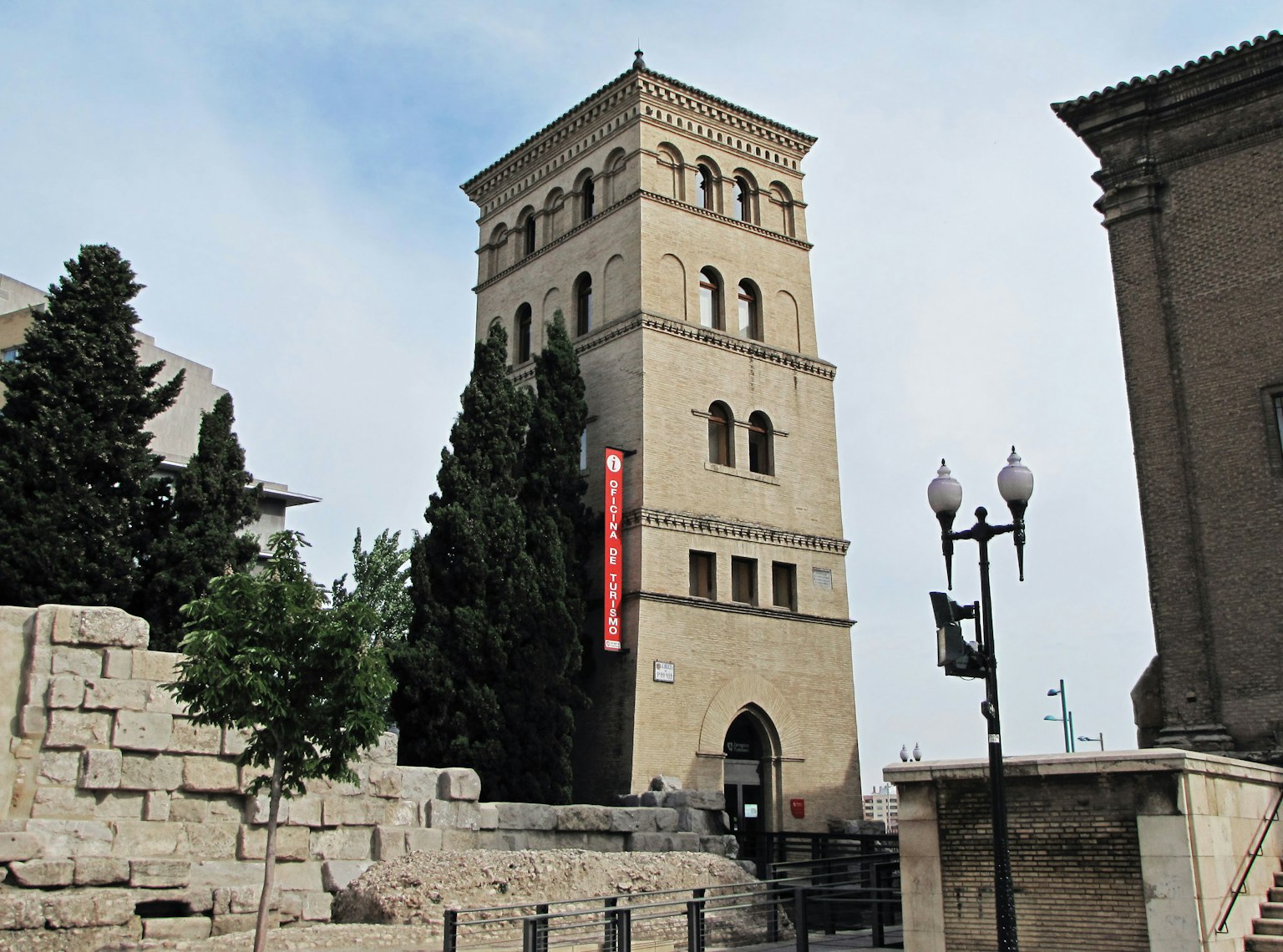 Torre de piedra histórica con vegetación y farolas cercanas