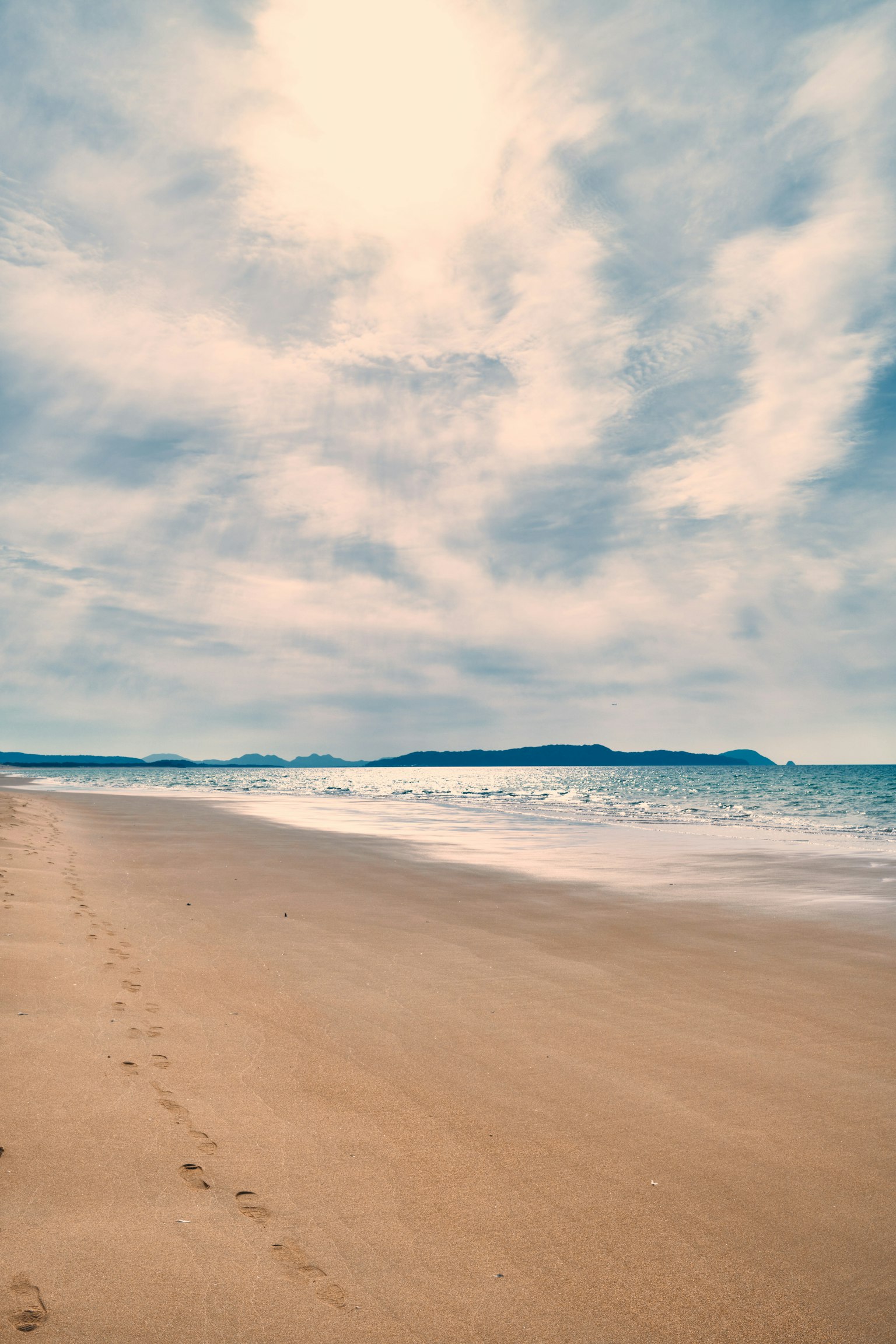 ทิวทัศน์ชายหาดที่เงียบสงบมีรอยเท้าบนทรายและคลื่นอ่อน