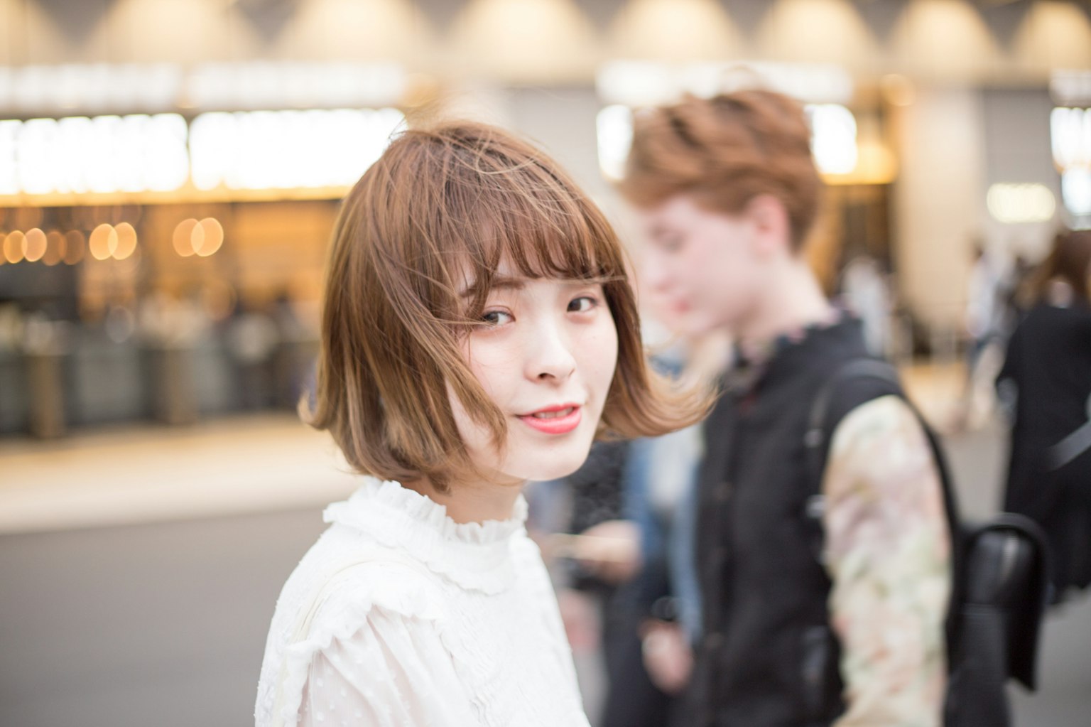 A woman with a distinctive hairstyle smiling at the camera with people walking in the background