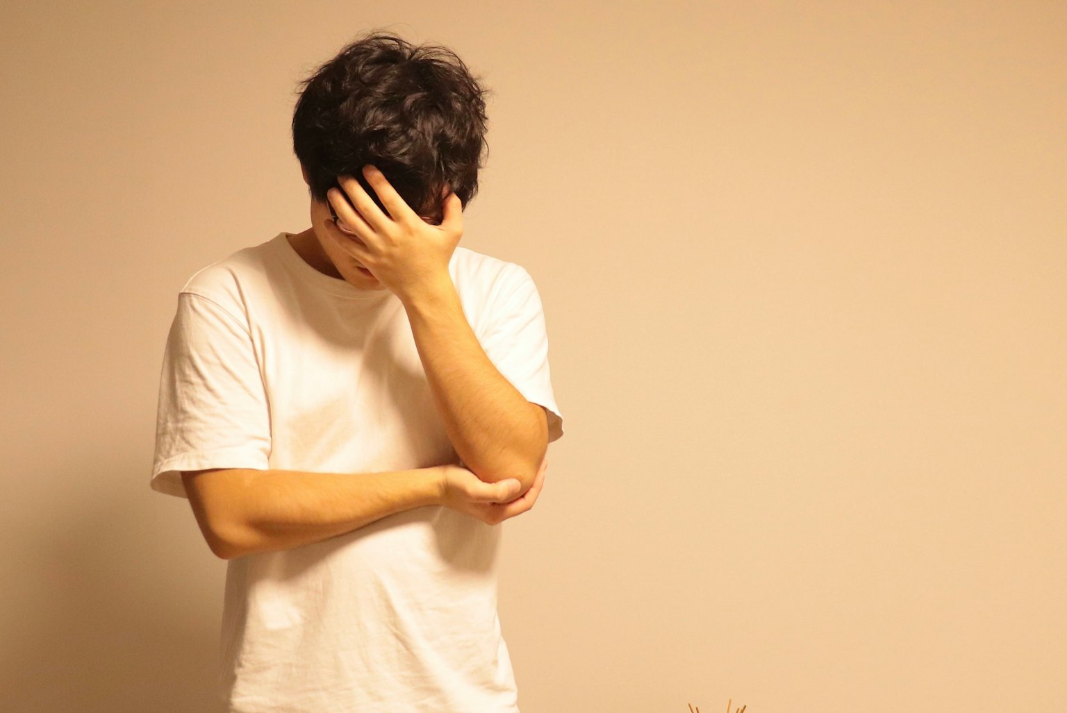 ชายคนหนึ่งปิดหน้าด้วยมือของเขาอยู่หน้าพื้นหลังสีอ่อนในโทนที่นุ่มนวล