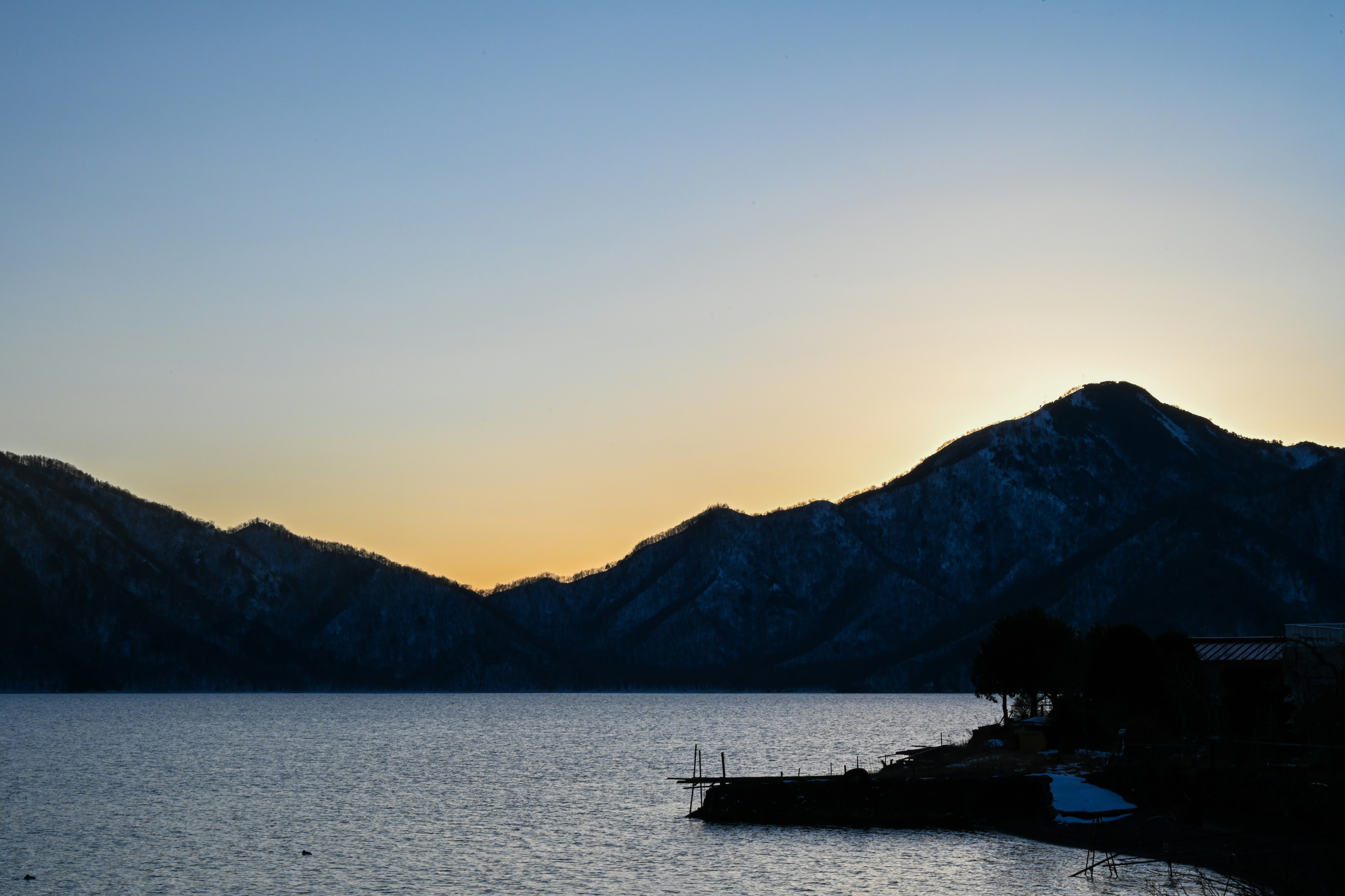 夕焼けの湖畔に浮かぶ小舟と山並み