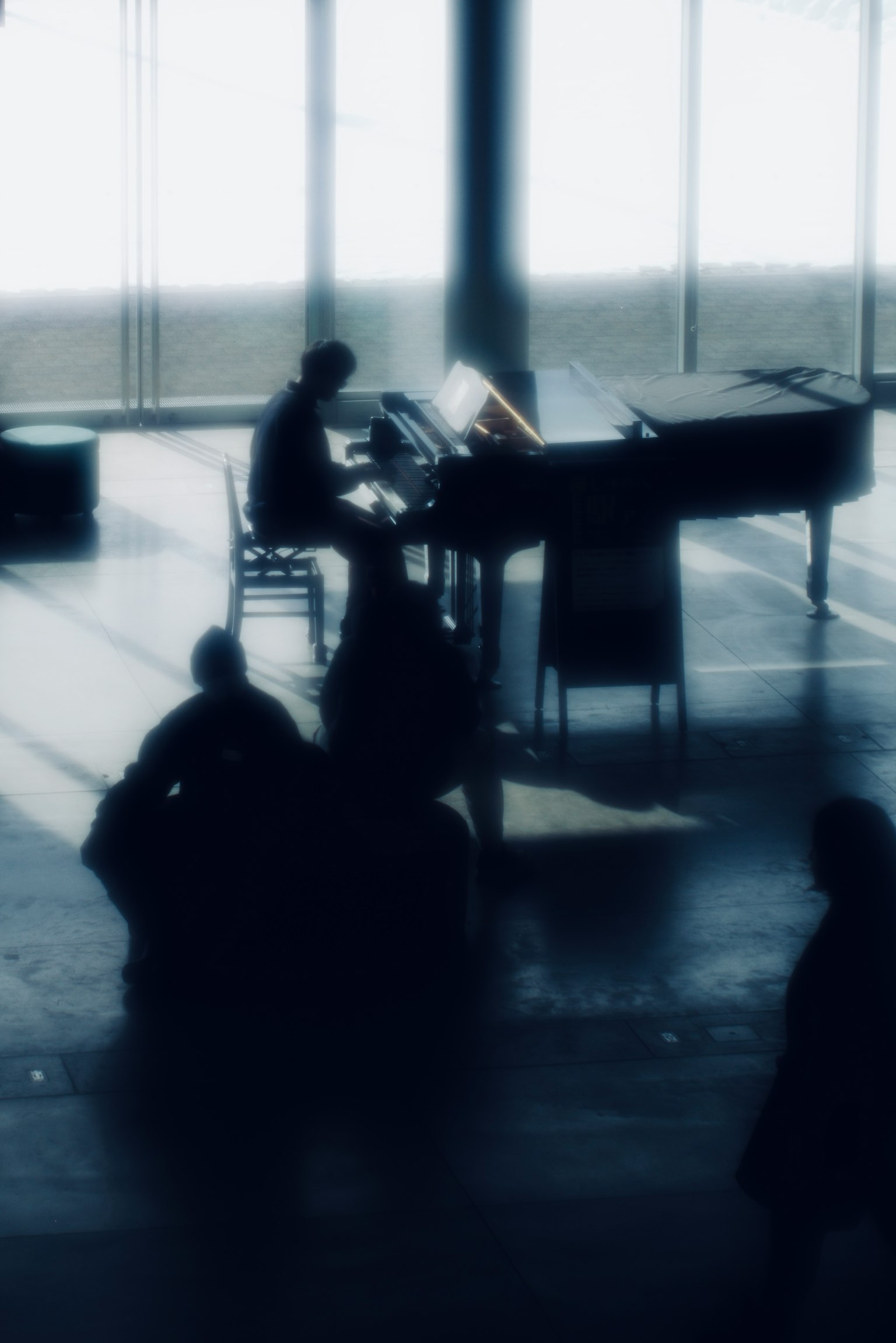 Eine Person, die Klavier spielt, in einem hellen Raum mit Silhouetten im Vordergrund
