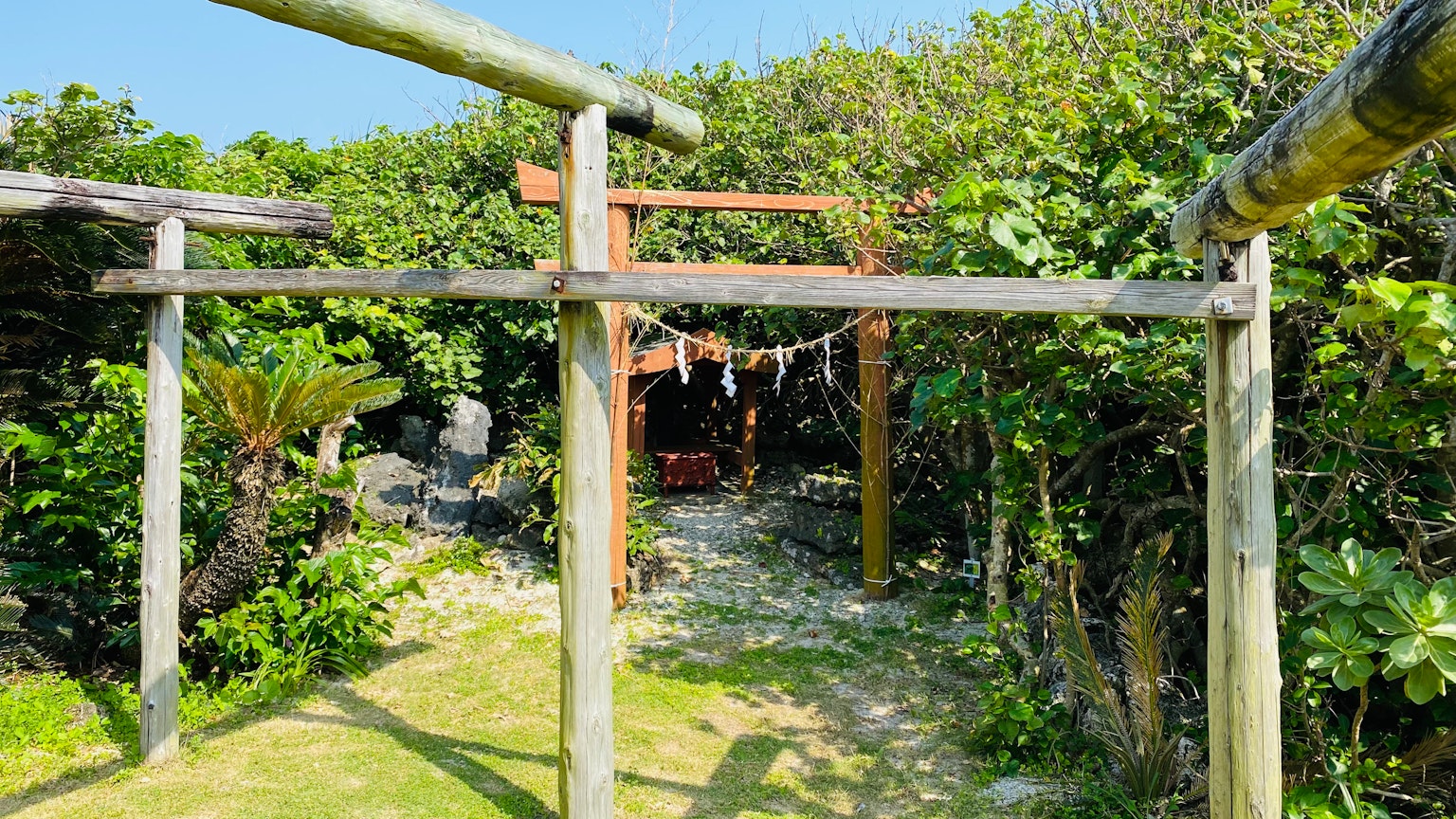 Wooden archway leading into a lush garden with a small cabin in the background