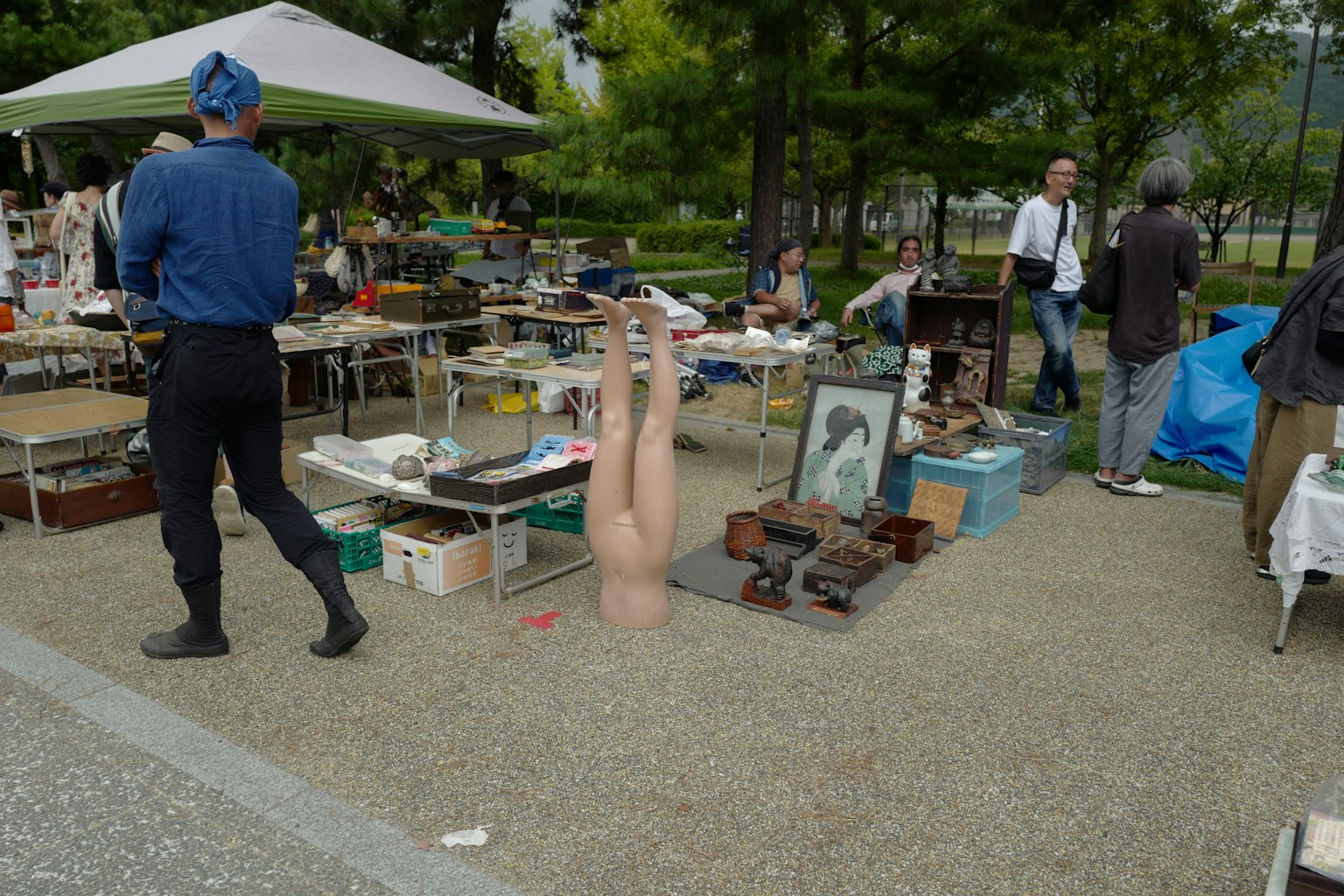 Outdoor market scene with various items for sale and mannequin legs protruding from the ground