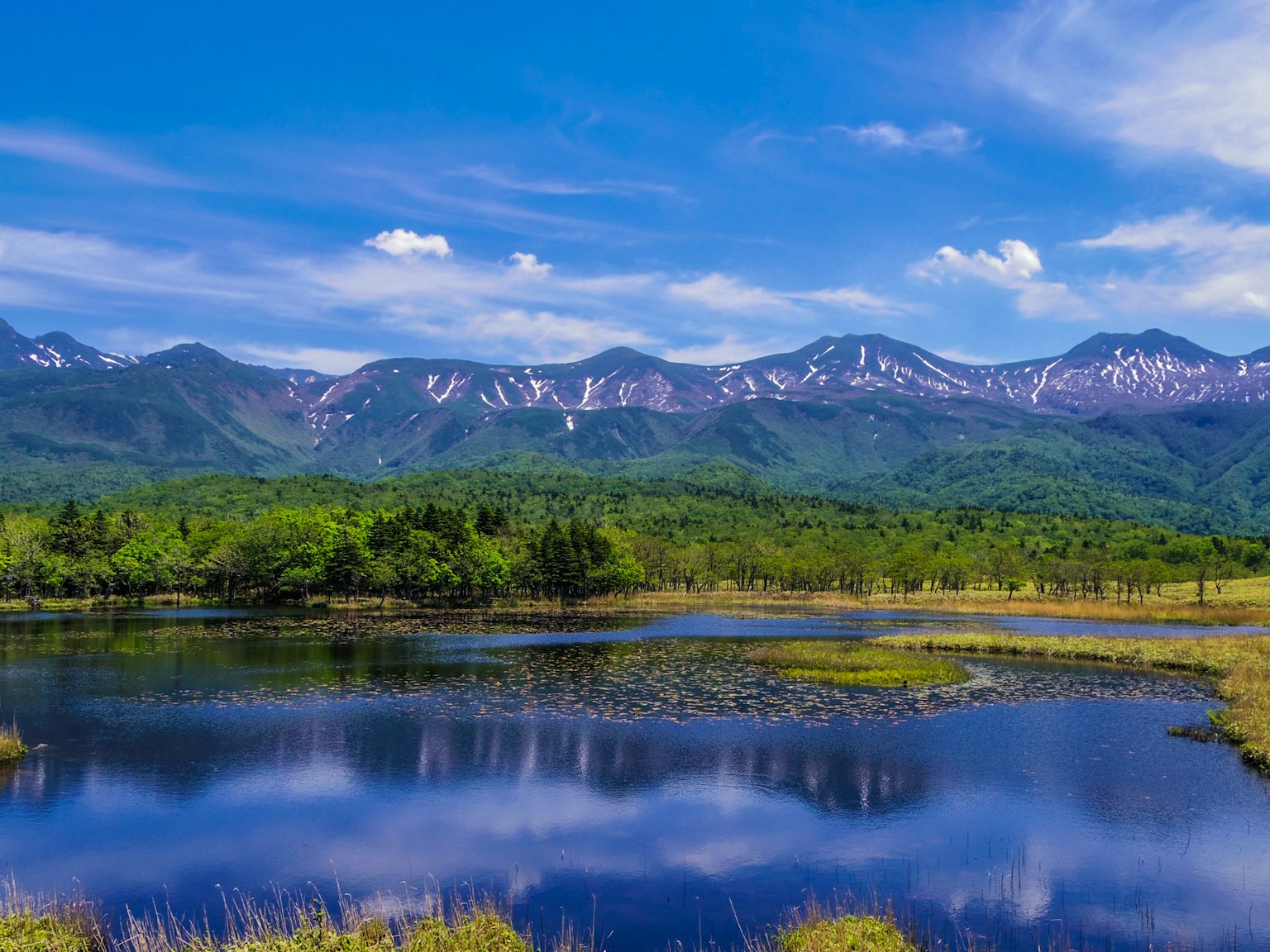 ทิวทัศน์ที่สวยงามของทะเลสาบที่สะท้อนภูเขาที่มีหิมะปกคลุมใต้ท้องฟ้าสีฟ้า