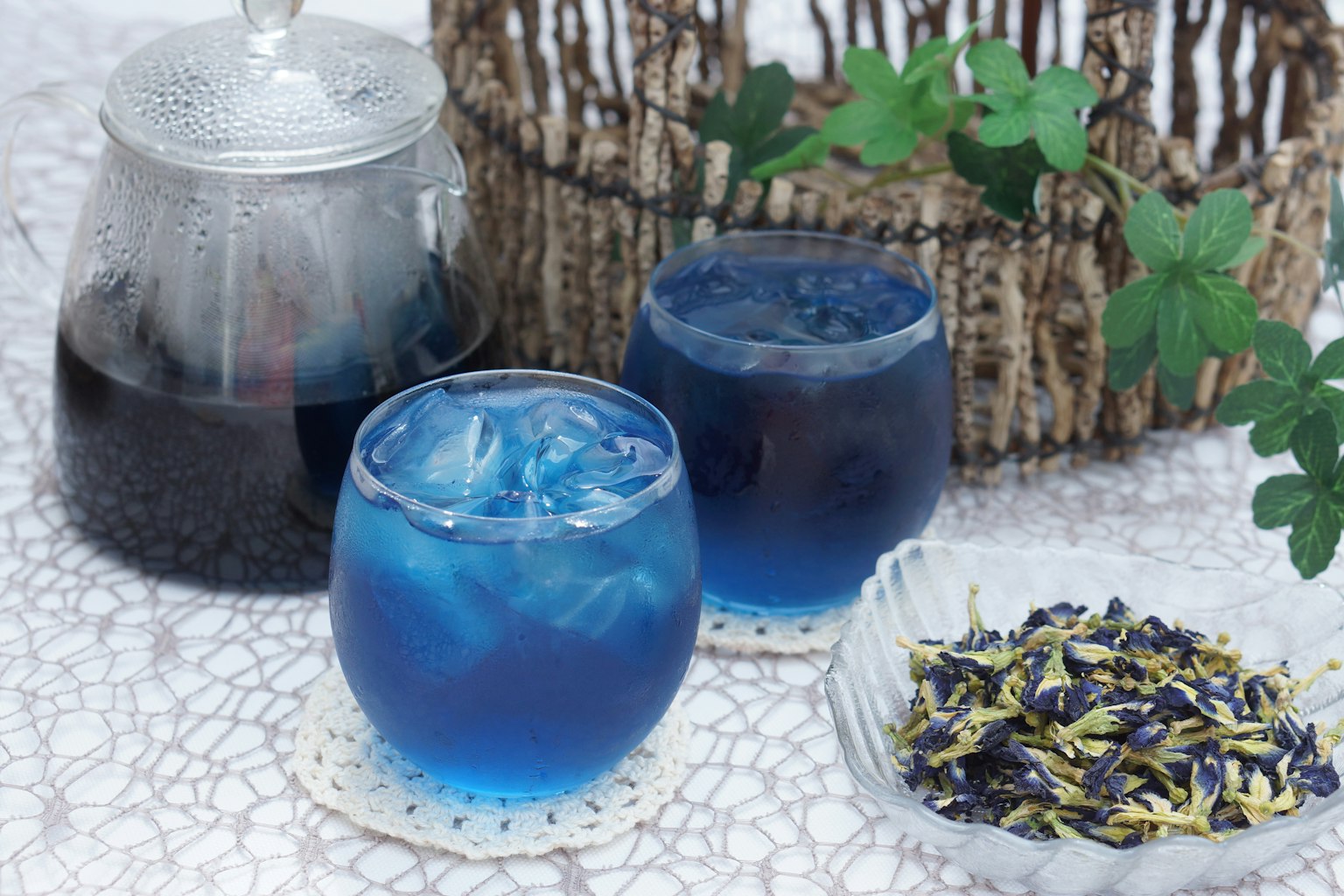 Deux verres de boisson bleue avec de la glace à côté d'une théière et de fleurs séchées