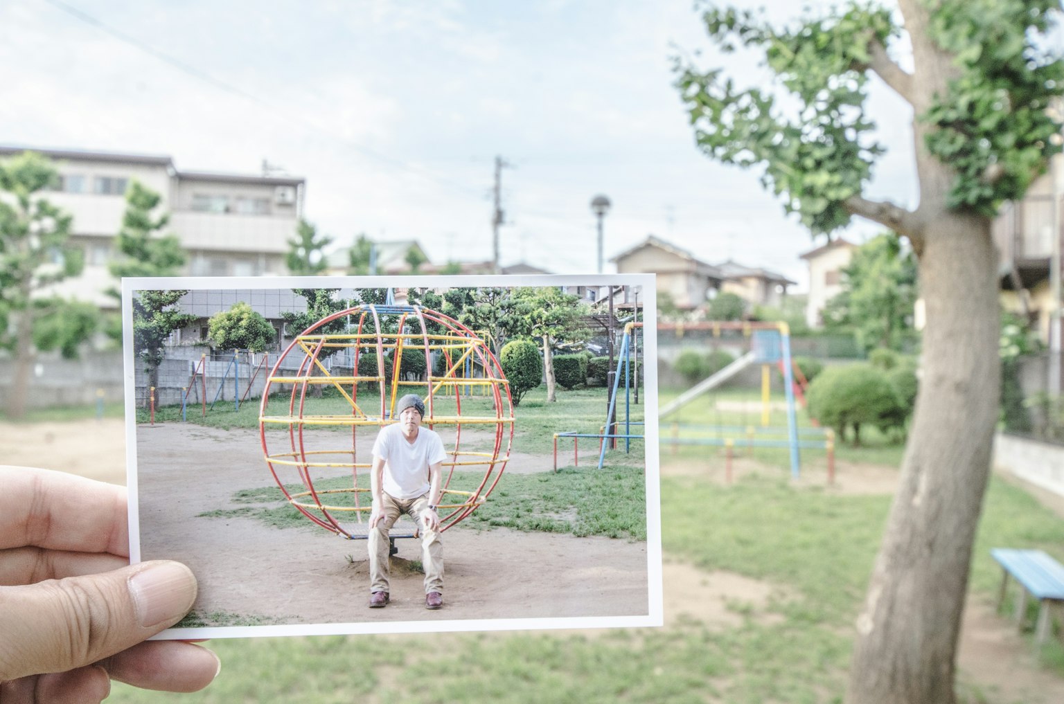 Mano che tiene una foto di un bambino che gioca in un parco con attrezzature per il gioco