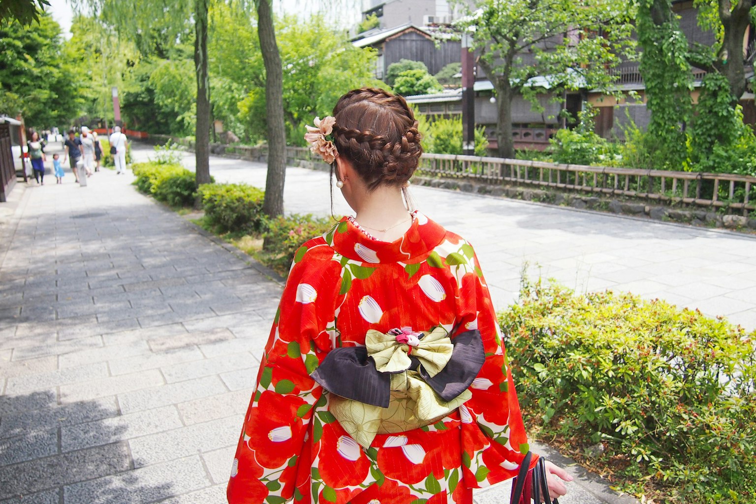 Frau, die in einem roten Blumenkimono mit einem schwarzen Obi geht