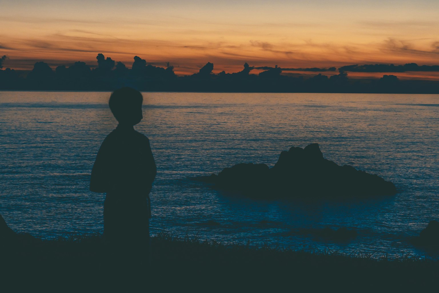 Silueta de un niño observando el atardecer sobre el mar