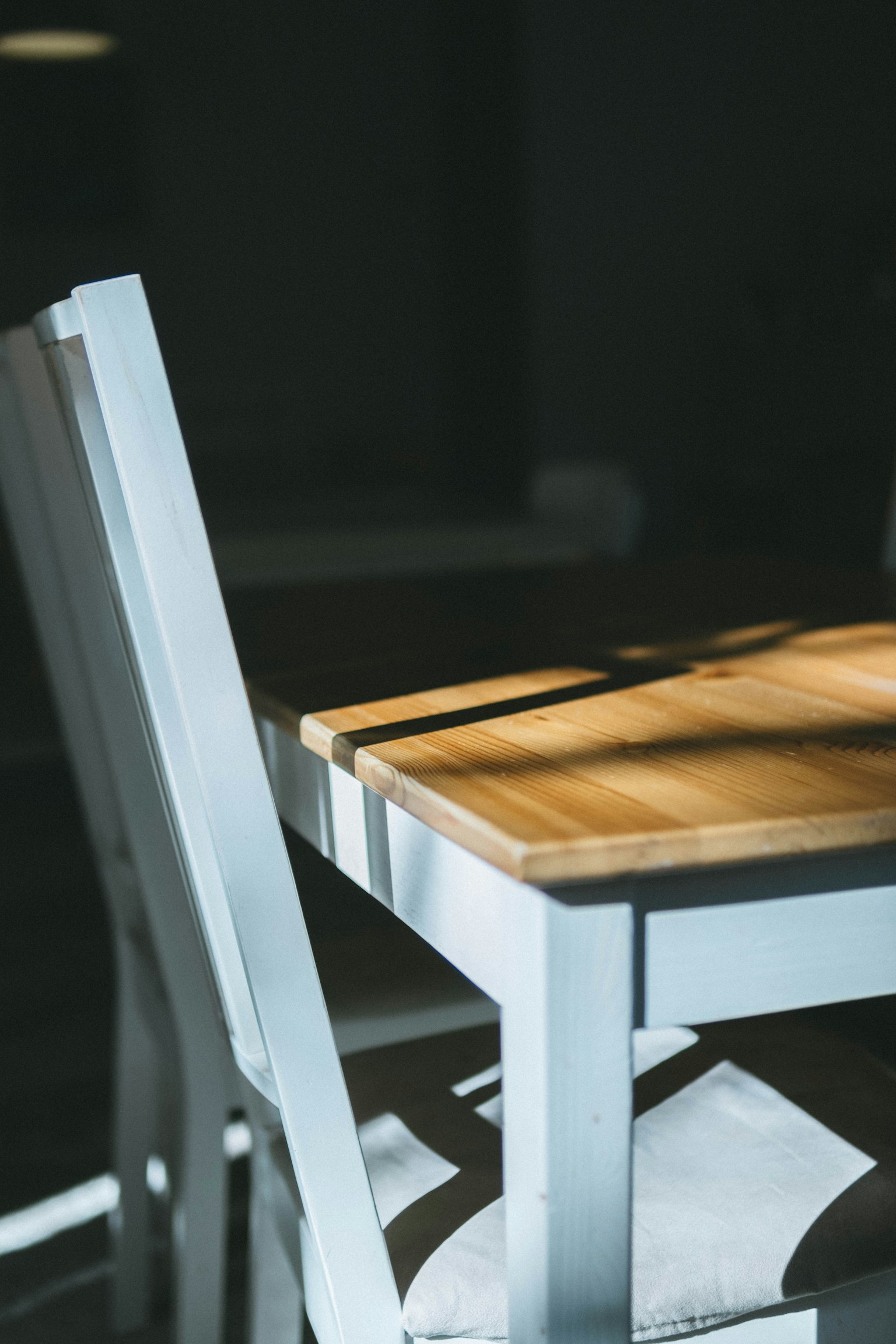 A close-up of a white chair and wooden table in a dimly lit room