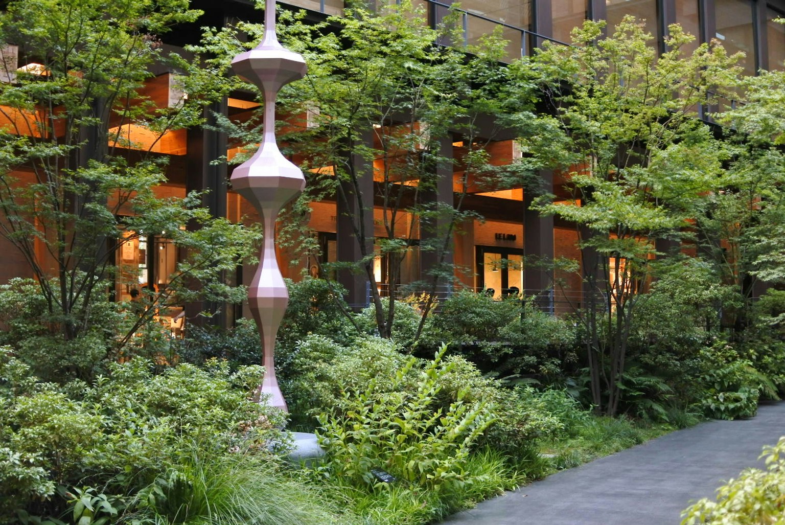 Einzigartige Skulptur in einem üppigen Garten mit Fenstern eines modernen Gebäudes