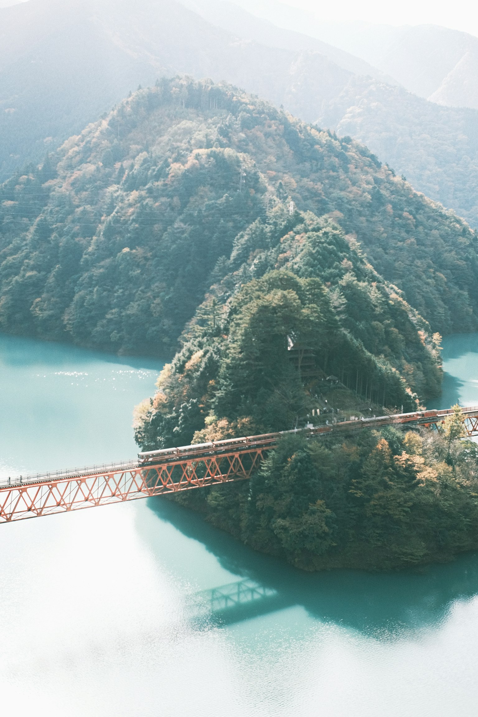 Eine rote Brücke überspannt einen blauen See, umgeben von grünen Bergen