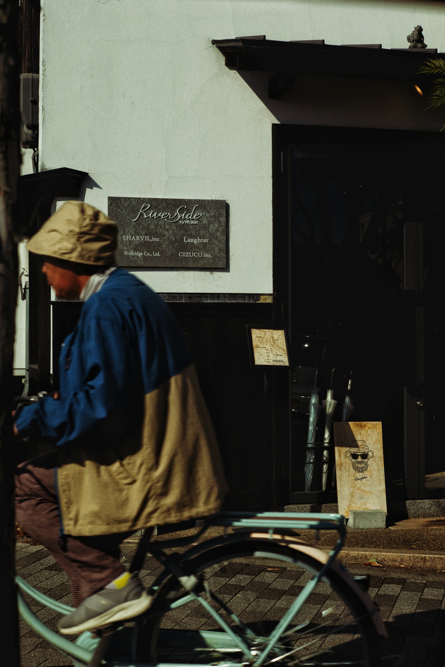 Một người đàn ông mặc đồ thường đi xe đạp qua một cửa hàng có biển hiệu ở phía sau