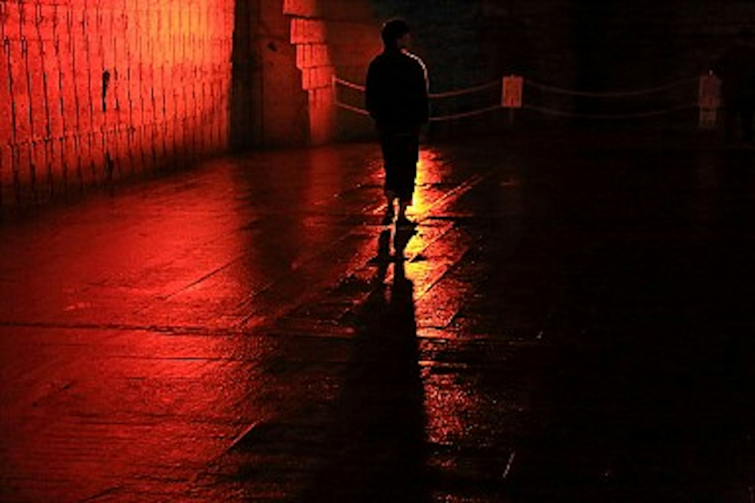 A silhouetted figure walking in a dark space illuminated by red light