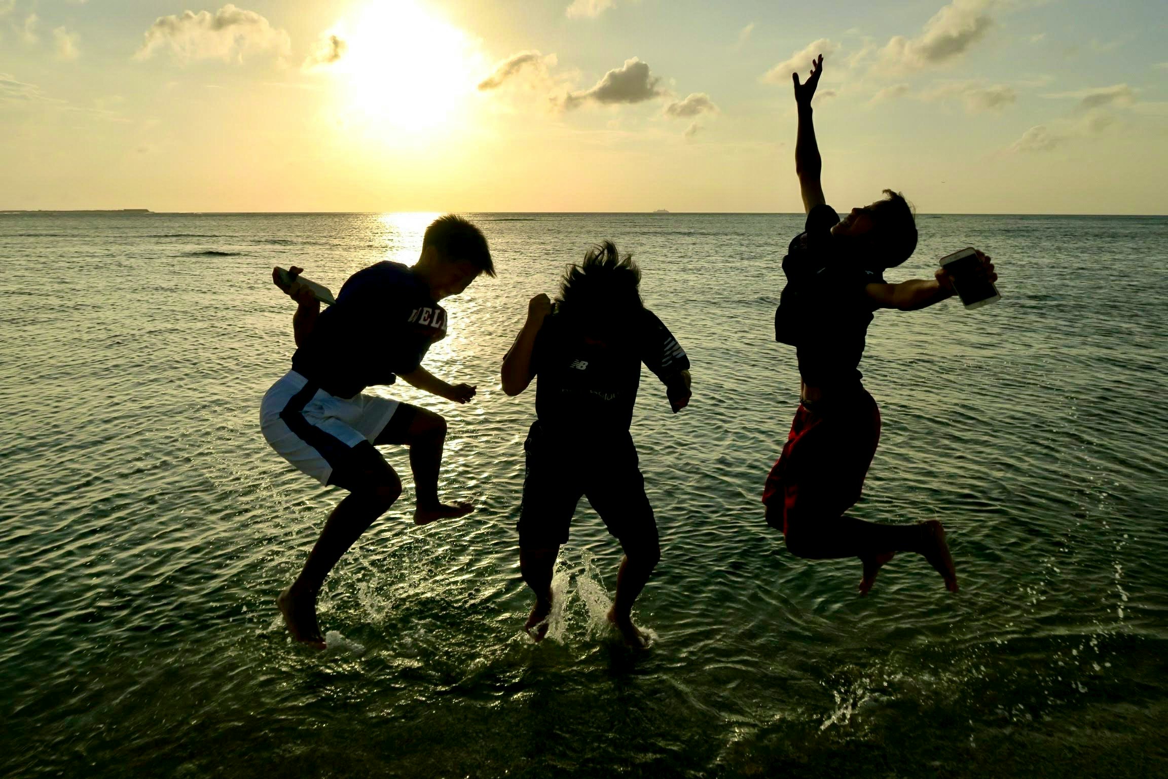 夕日に照らされた海辺でジャンプする若者たち