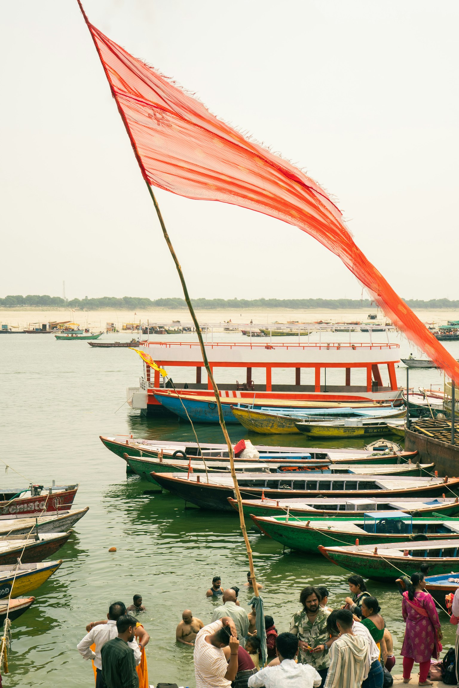 Un grand drapeau rouge près de la rivière avec des bateaux colorés visibles