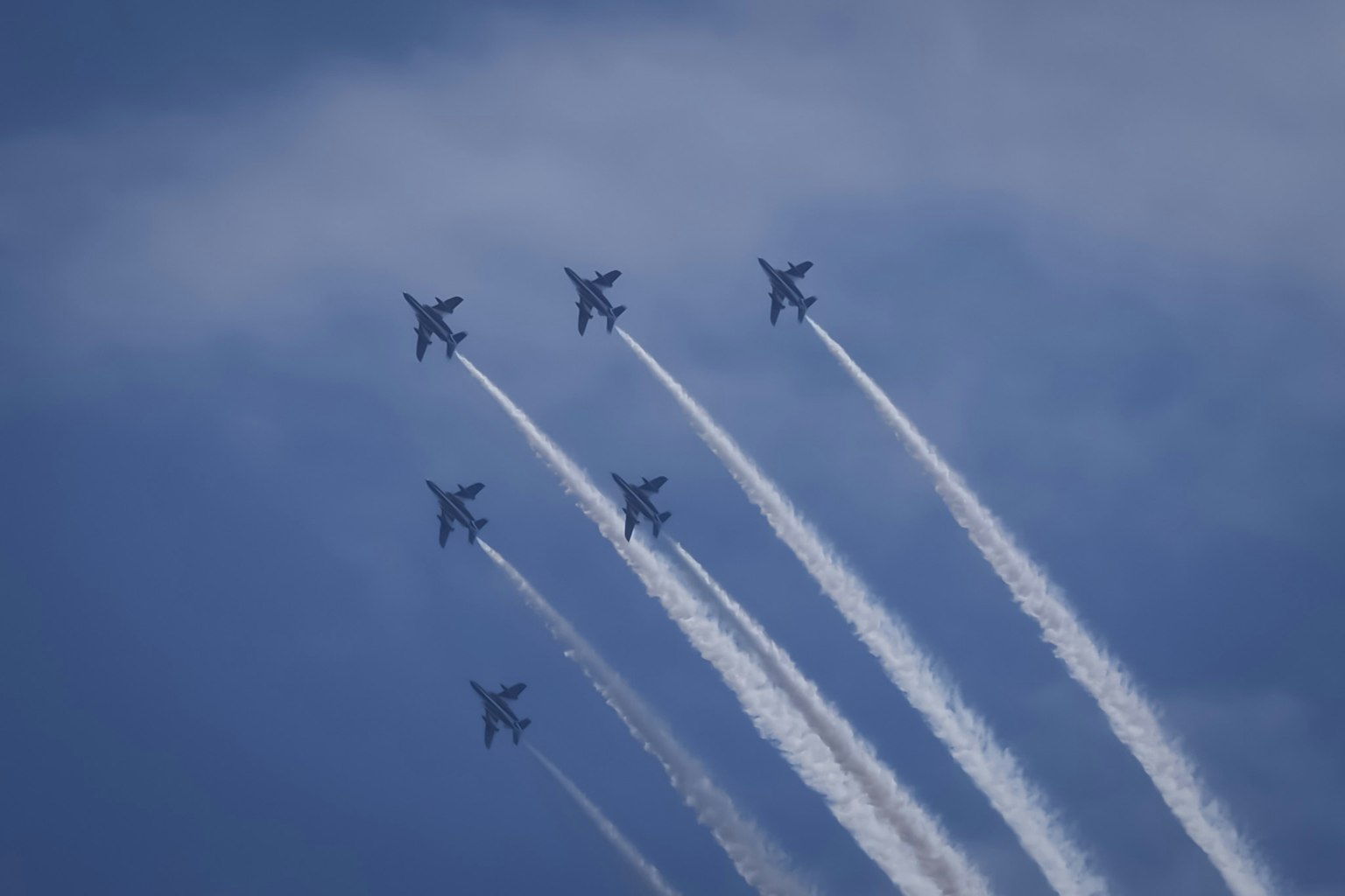 Formasi enam jet tempur yang naik ke langit biru meninggalkan jejak putih