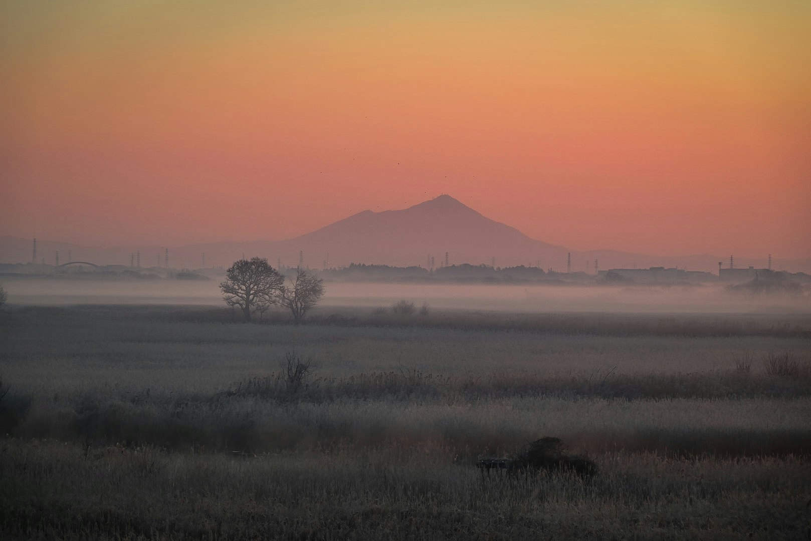 霧のかかった田園と遠くの山並みの夕景
