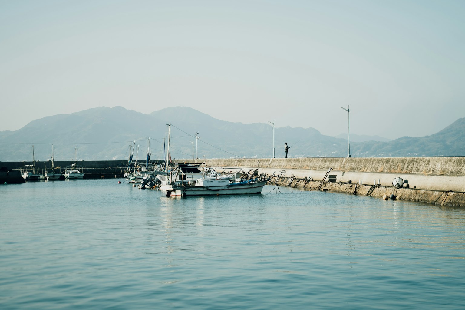 Escena de puerto tranquila con pequeños botes y superficie de agua tranquila montañas al fondo
