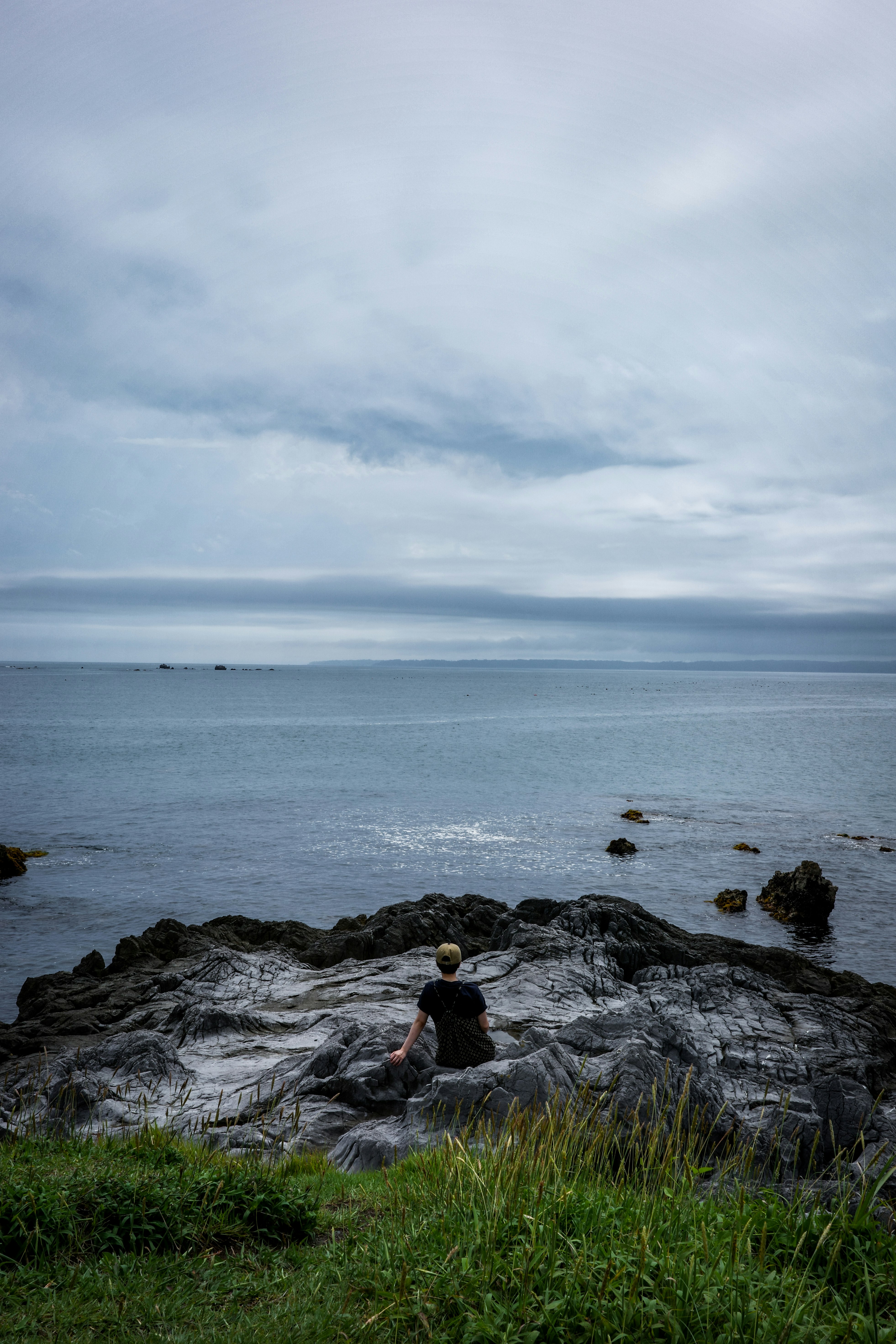 une personne assise sur des rochers au bord de l’océan et l’horizon au loin