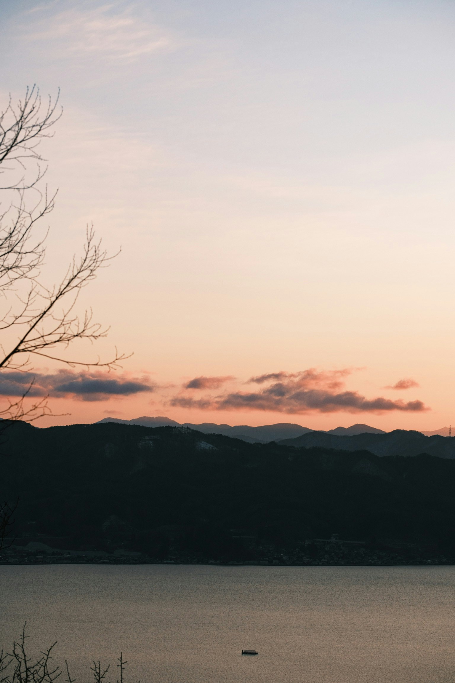 夕陽下的山脈剪影與寧靜湖面，遠處有一艘小船