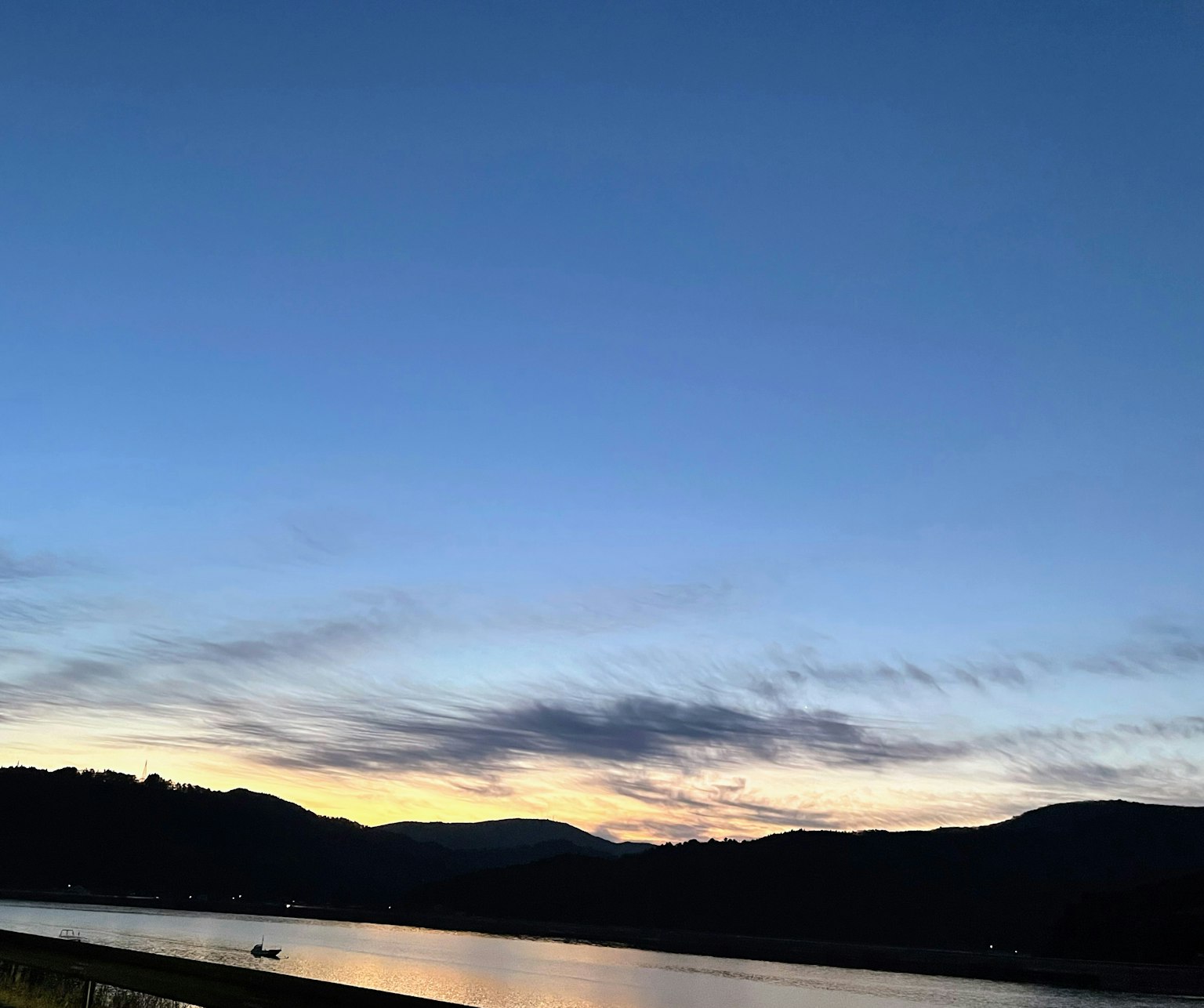Atardecer sobre un río con montañas al fondo cielo azul con nubes