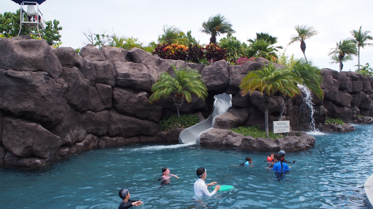 Bambini che giocano in una piscina con uno scivolo d'acqua e piante tropicali lussureggianti