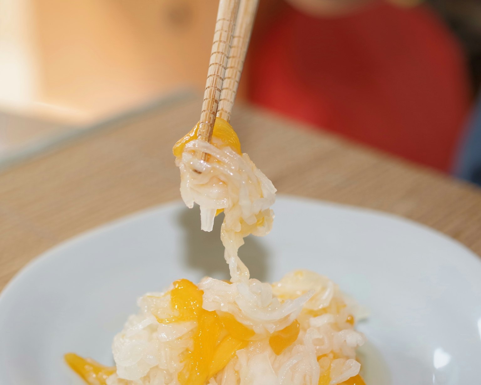 Une main soulevant un dessert en gelée orange et blanche avec des baguettes
