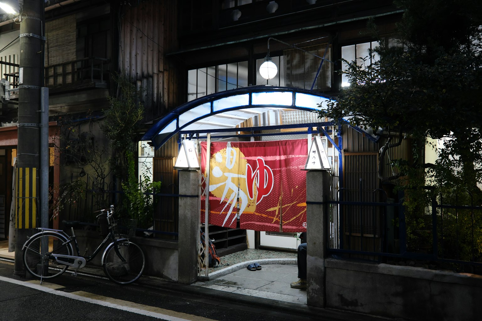 Entrada japonesa tradicional por la noche con un noren rojo y una bicicleta