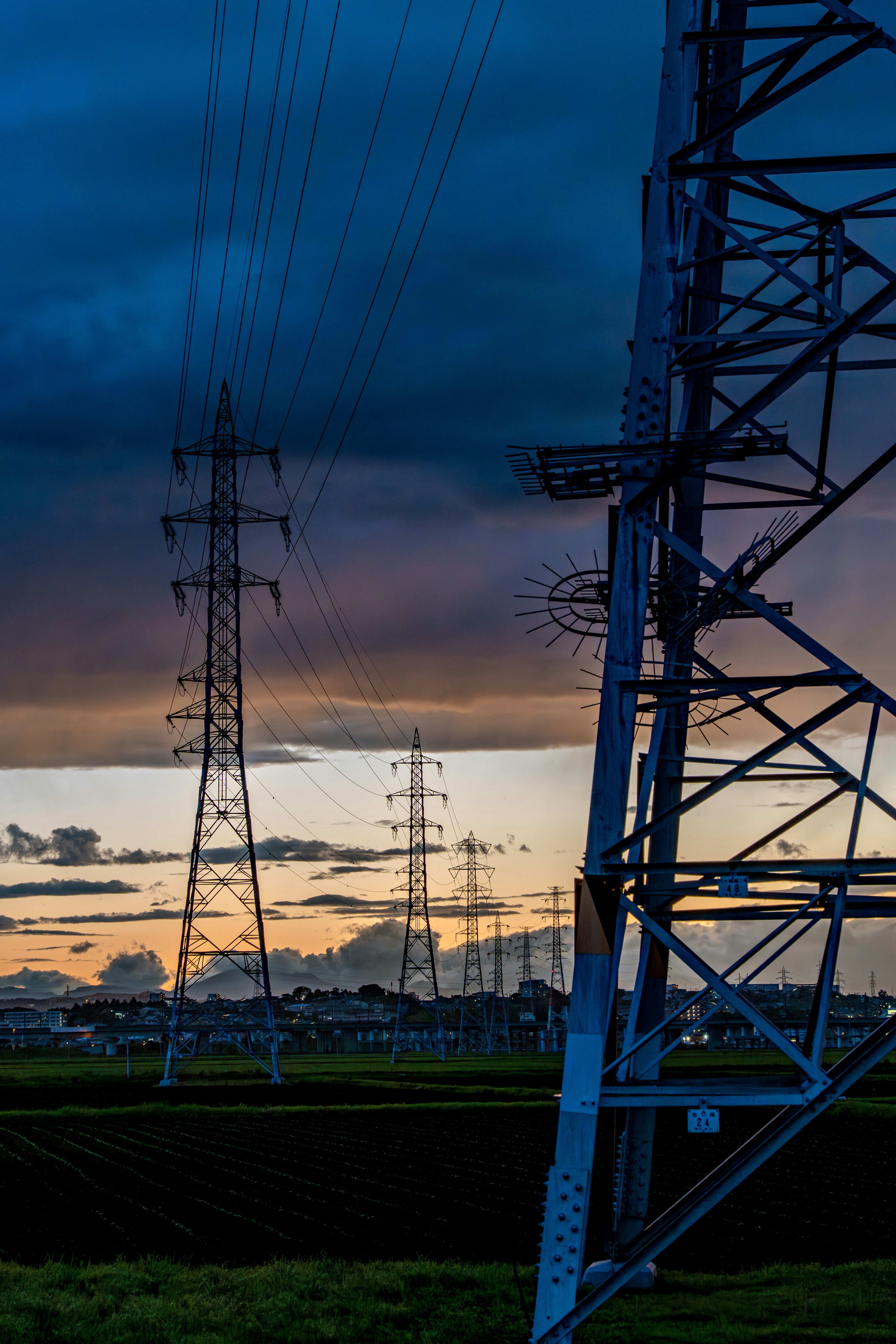 夕暮れの送電鉄塔と広がる田畑の風景