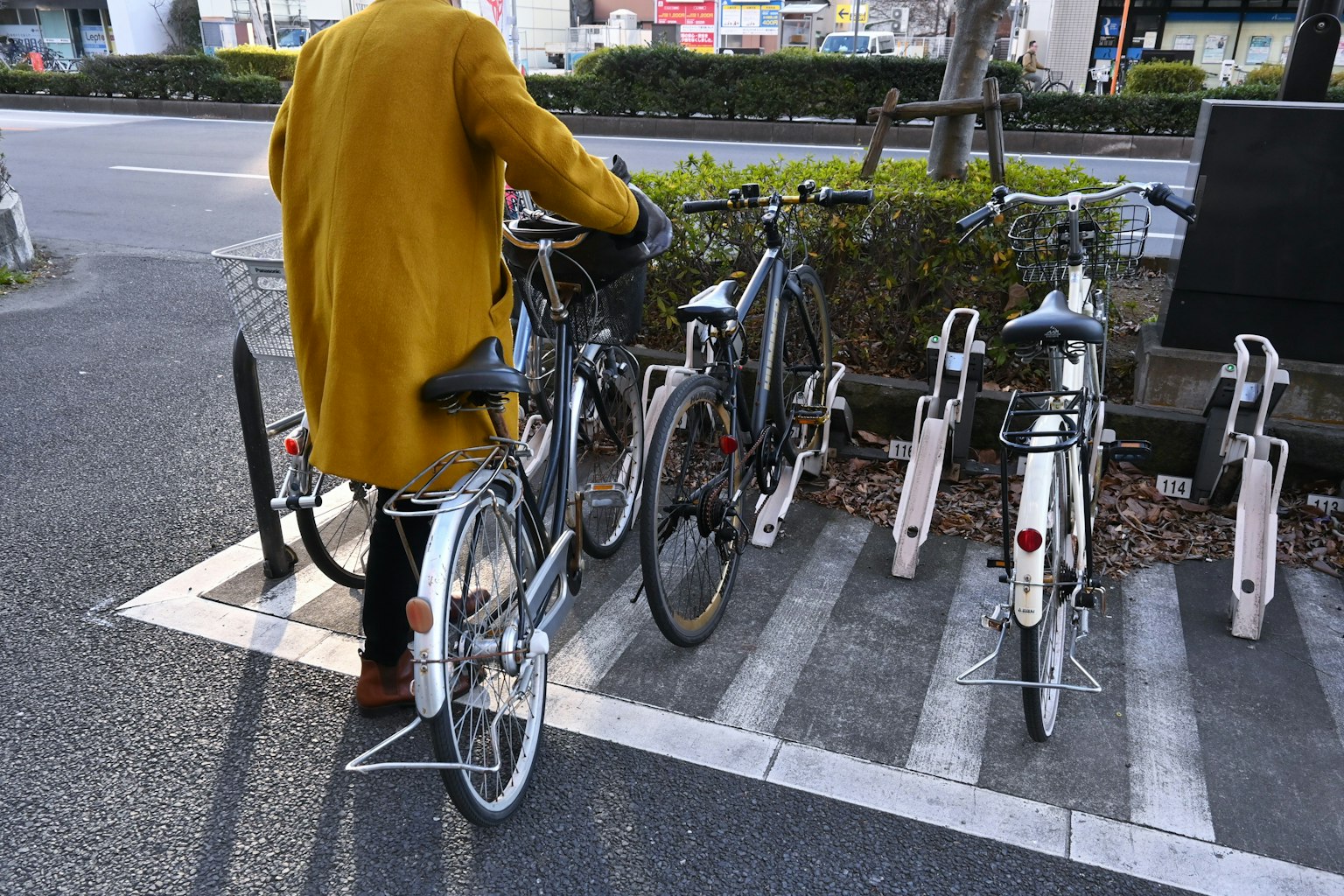 Persona aparcando una bicicleta en un estacionamiento para bicicletas con un abrigo amarillo