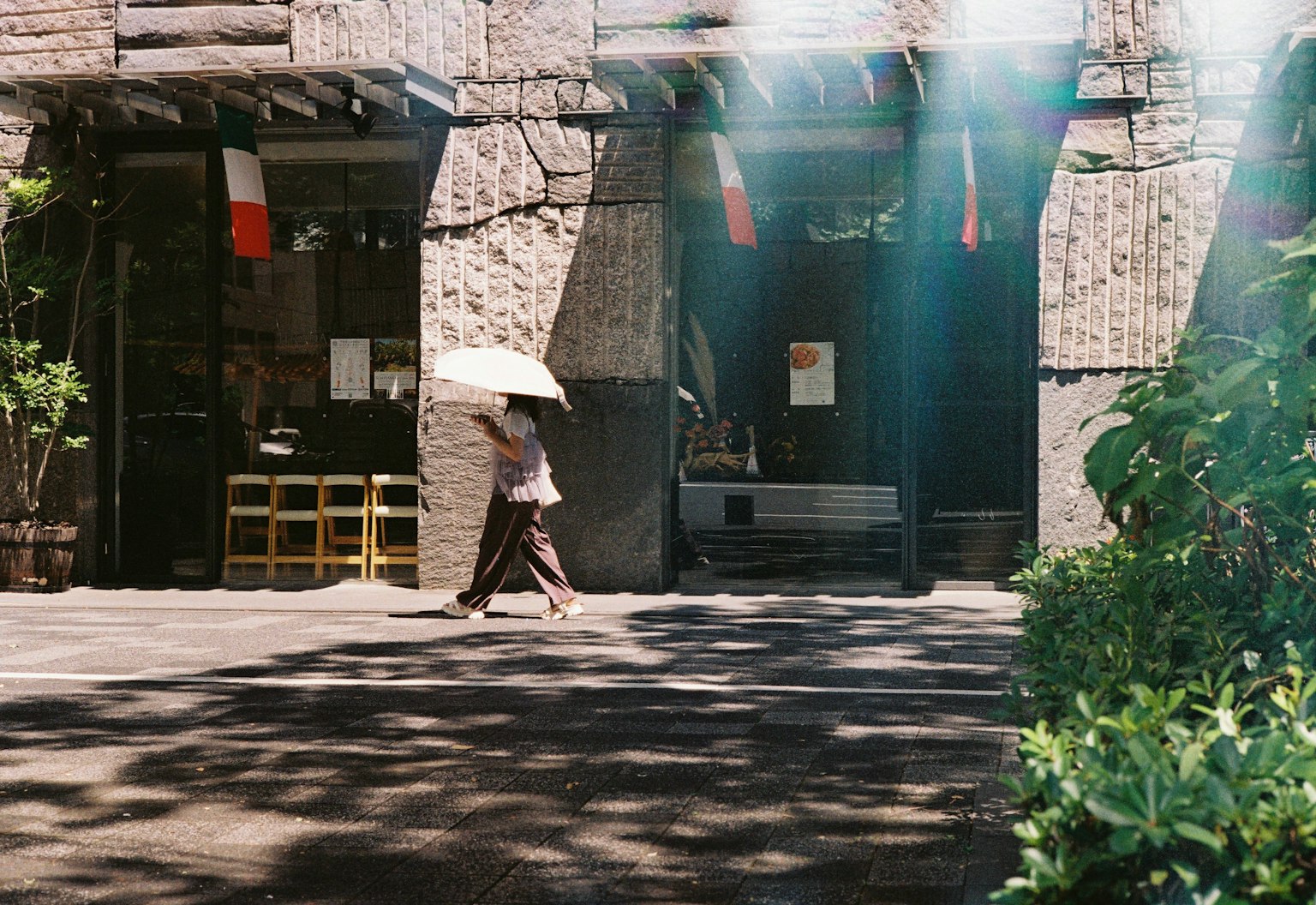 Seorang wanita berjalan dengan payung di depan bangunan batu