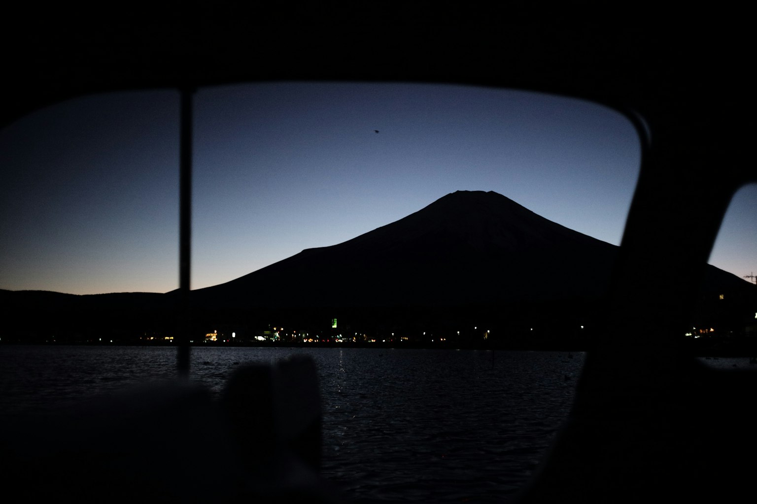 Silhouette d'une montagne à l'aube avec un lac et des lumières de ville