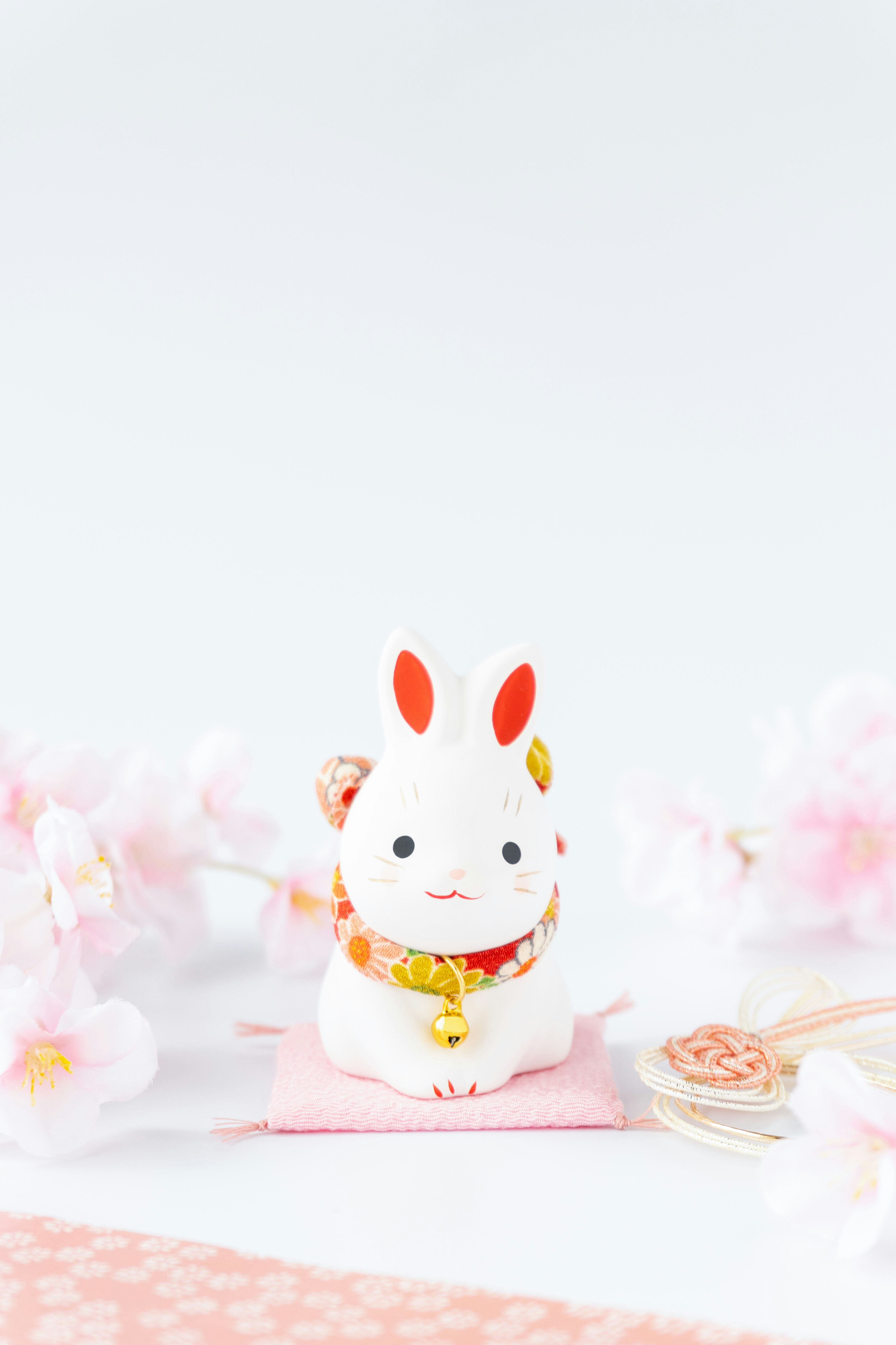 tượng thỏ may mắn màu trắng ngồi trên nền hồng với hoa anh đào phía sau