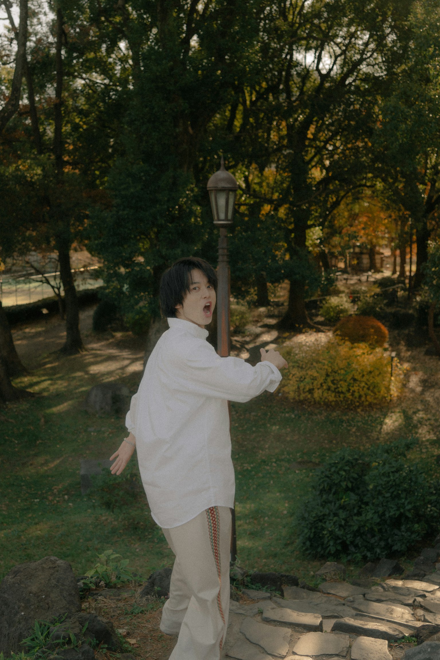 一位穿著白襯衫的年輕人在公園裡走向一盞路燈